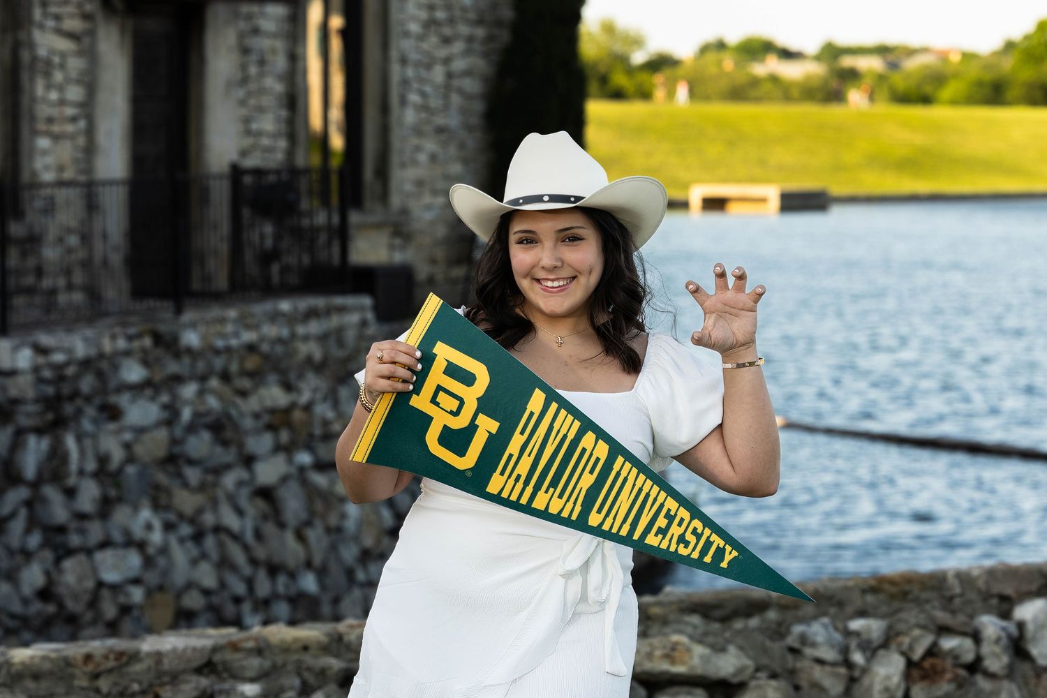 Baylor University pride shown with white dress, cowboy hat and school pennant by the water.