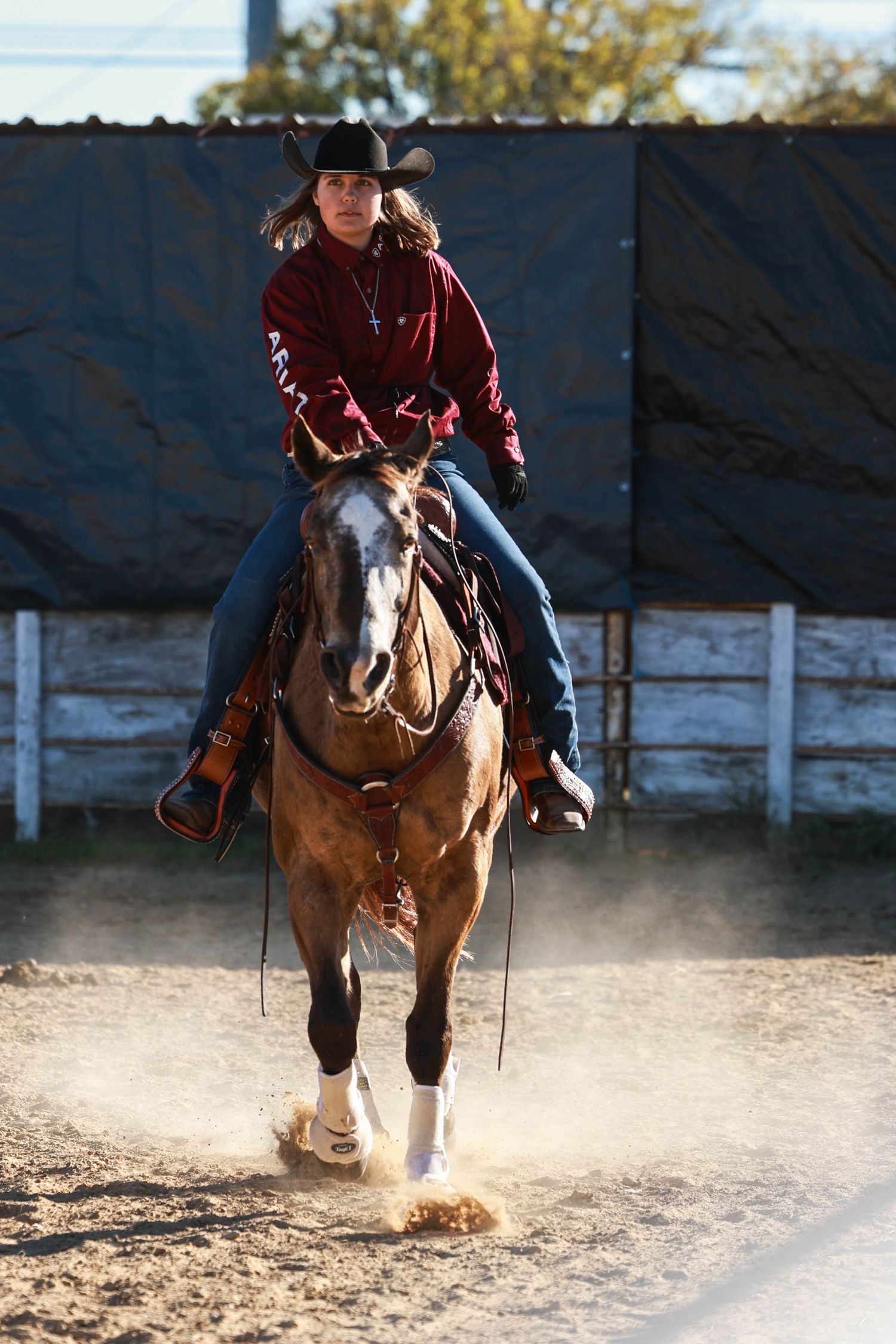 Western rider guides a paint horse through an indoor arena creating dust clouds.
