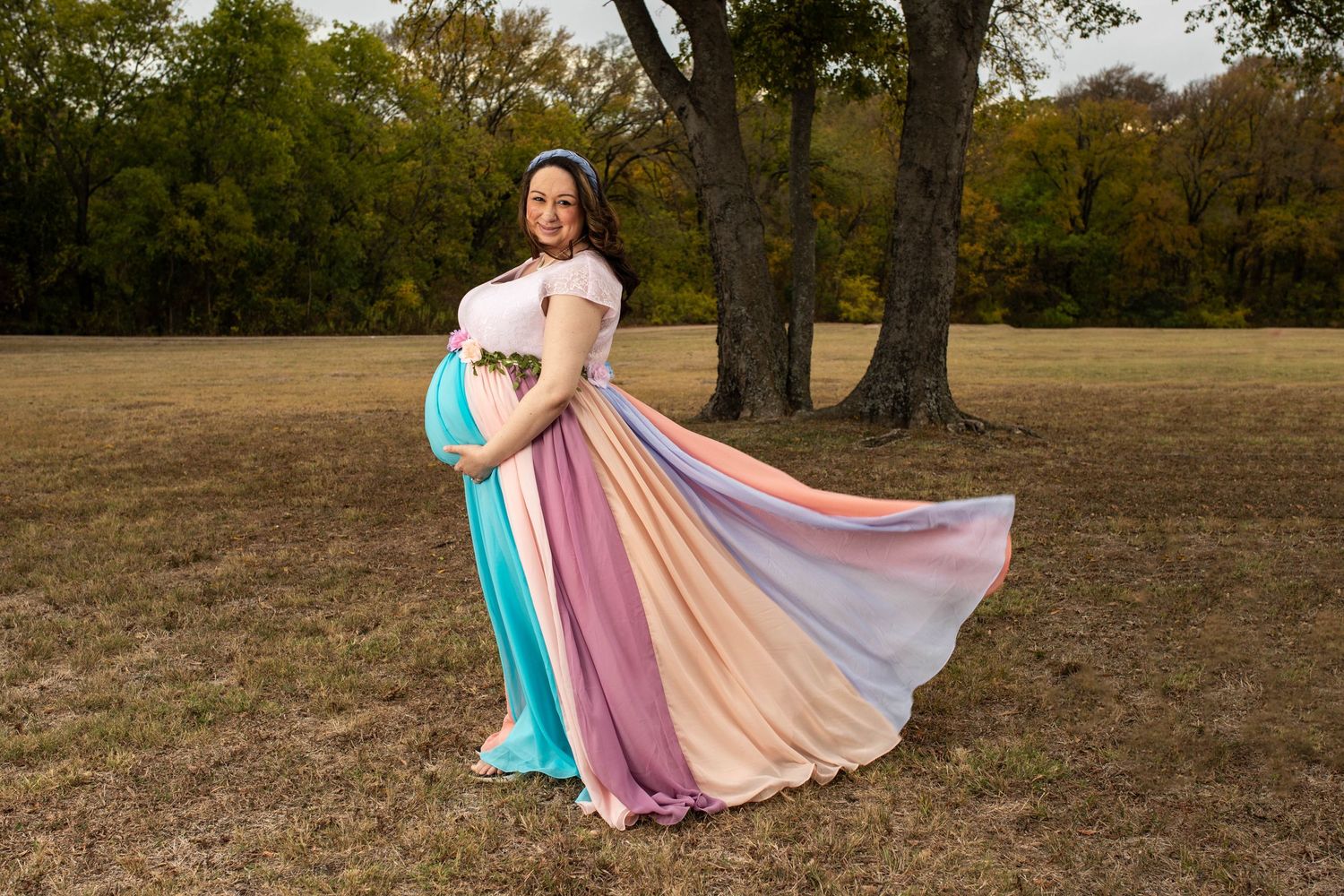 Person twirling in a flowing rainbow-colored dress in an autumn field.
