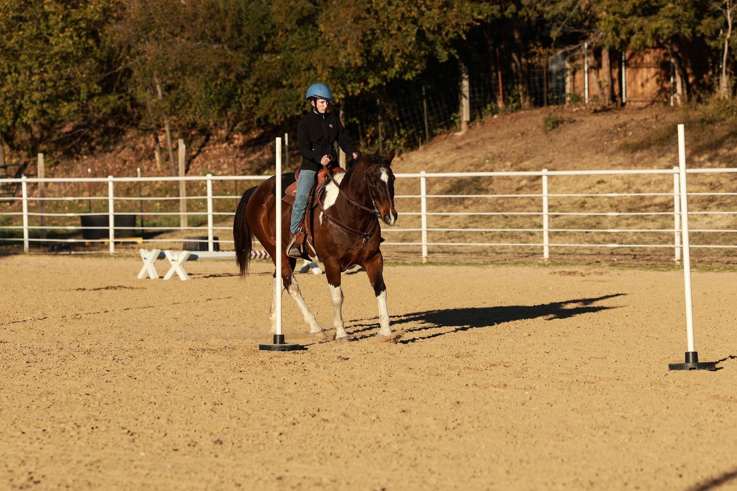 Horse and rider navigating around poles in a sandy arena during a competition event.