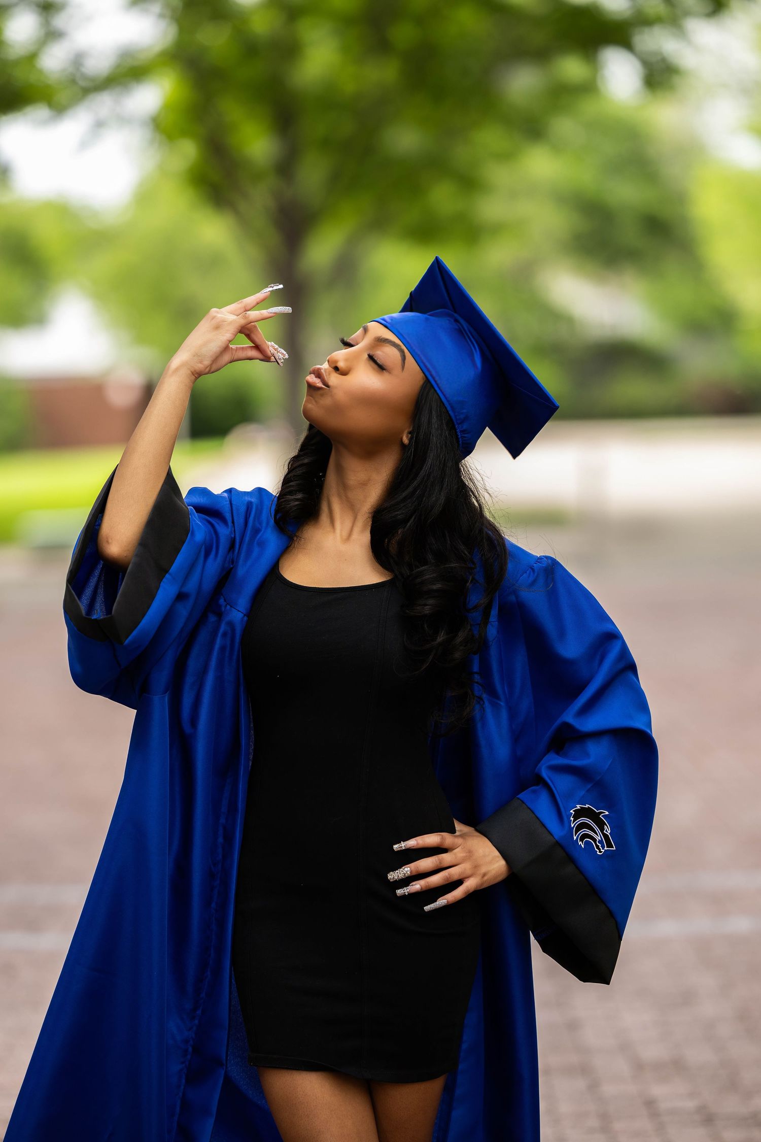 Graduate in royal blue cap and gown strikes a confident pose outdoors during commencement photo session.