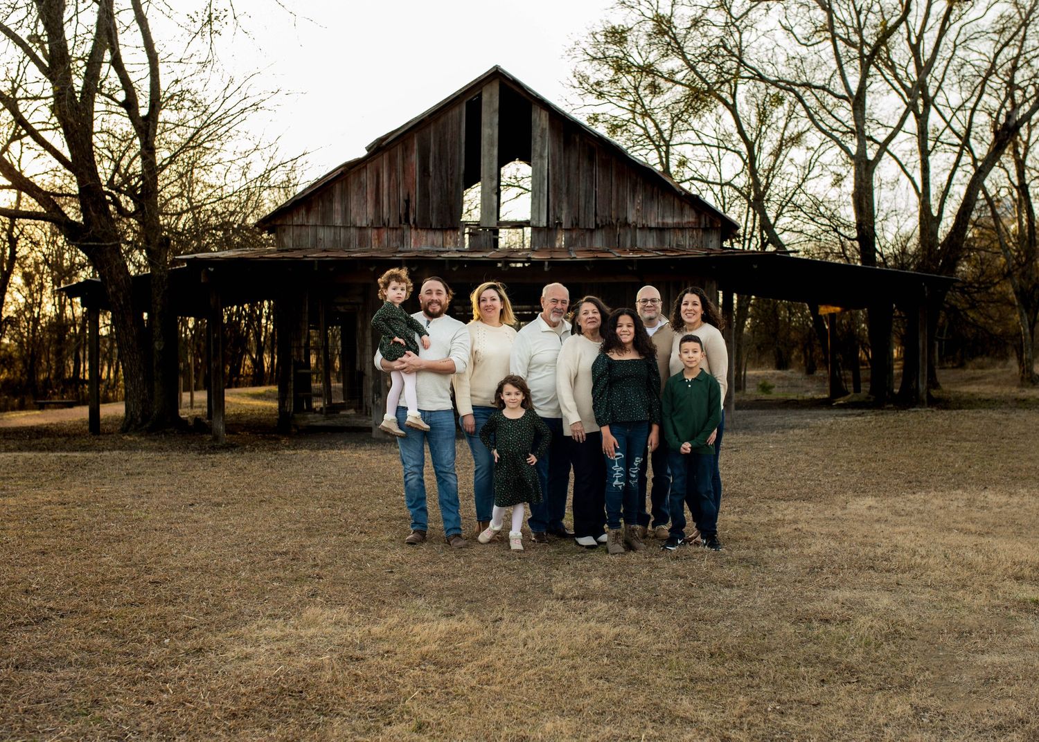 A group poses together in front of a rustic wooden barn structure at sunset.