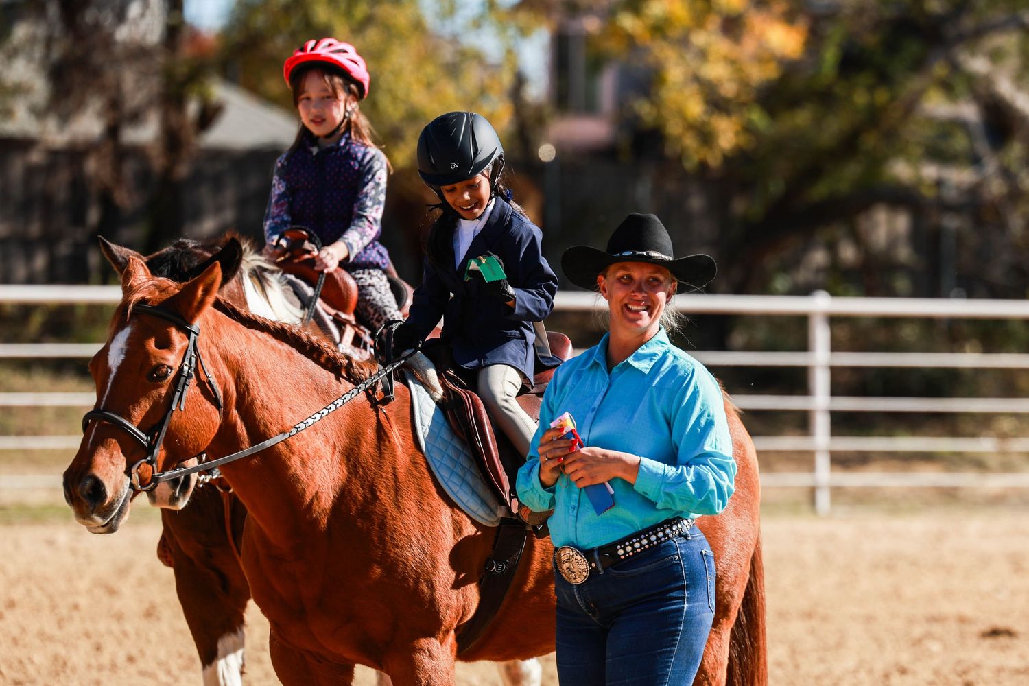 Riding lesson in progress with students on horseback in an outdoor arena.