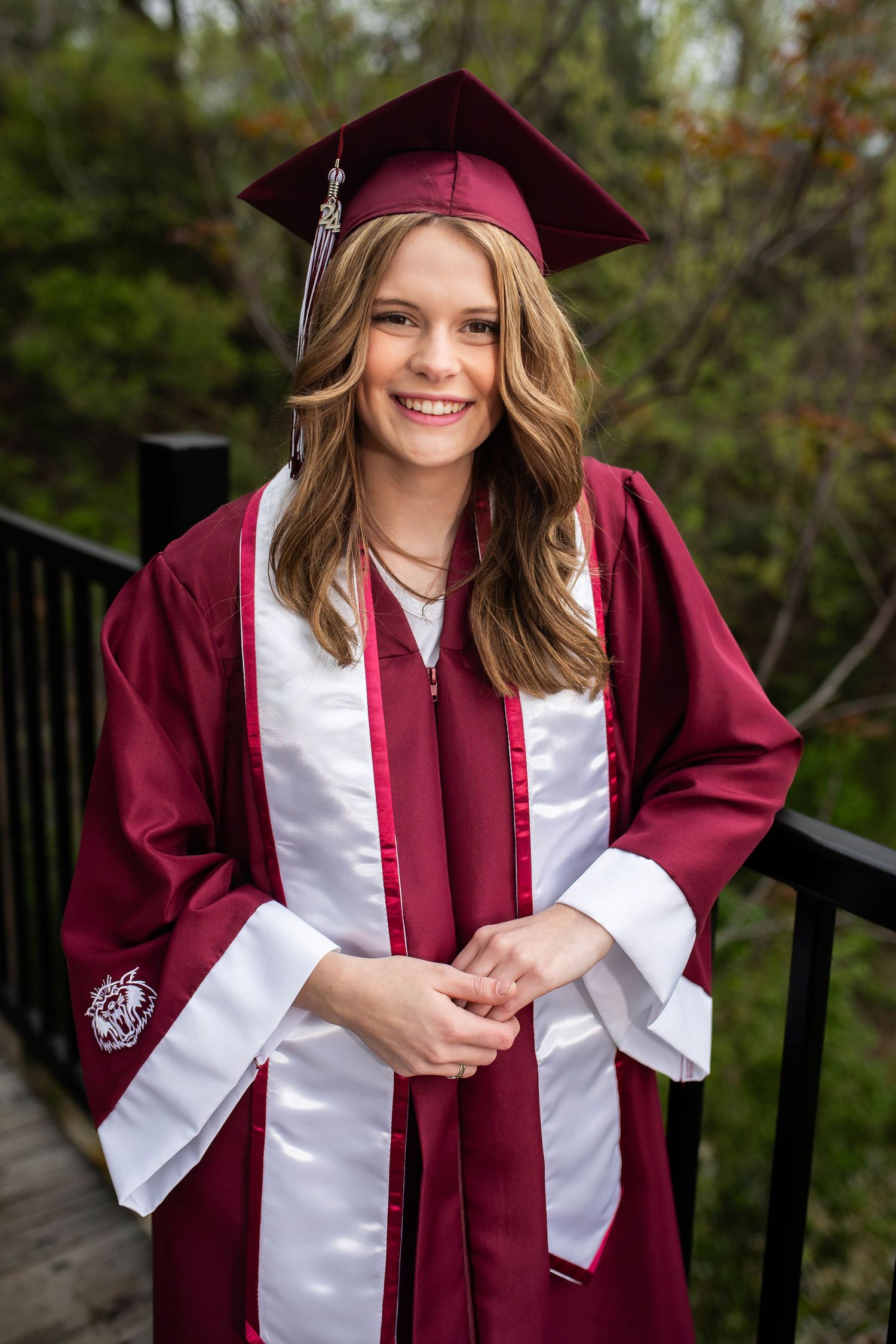 Graduate wearing maroon and white graduation regalia poses on outdoor deck.