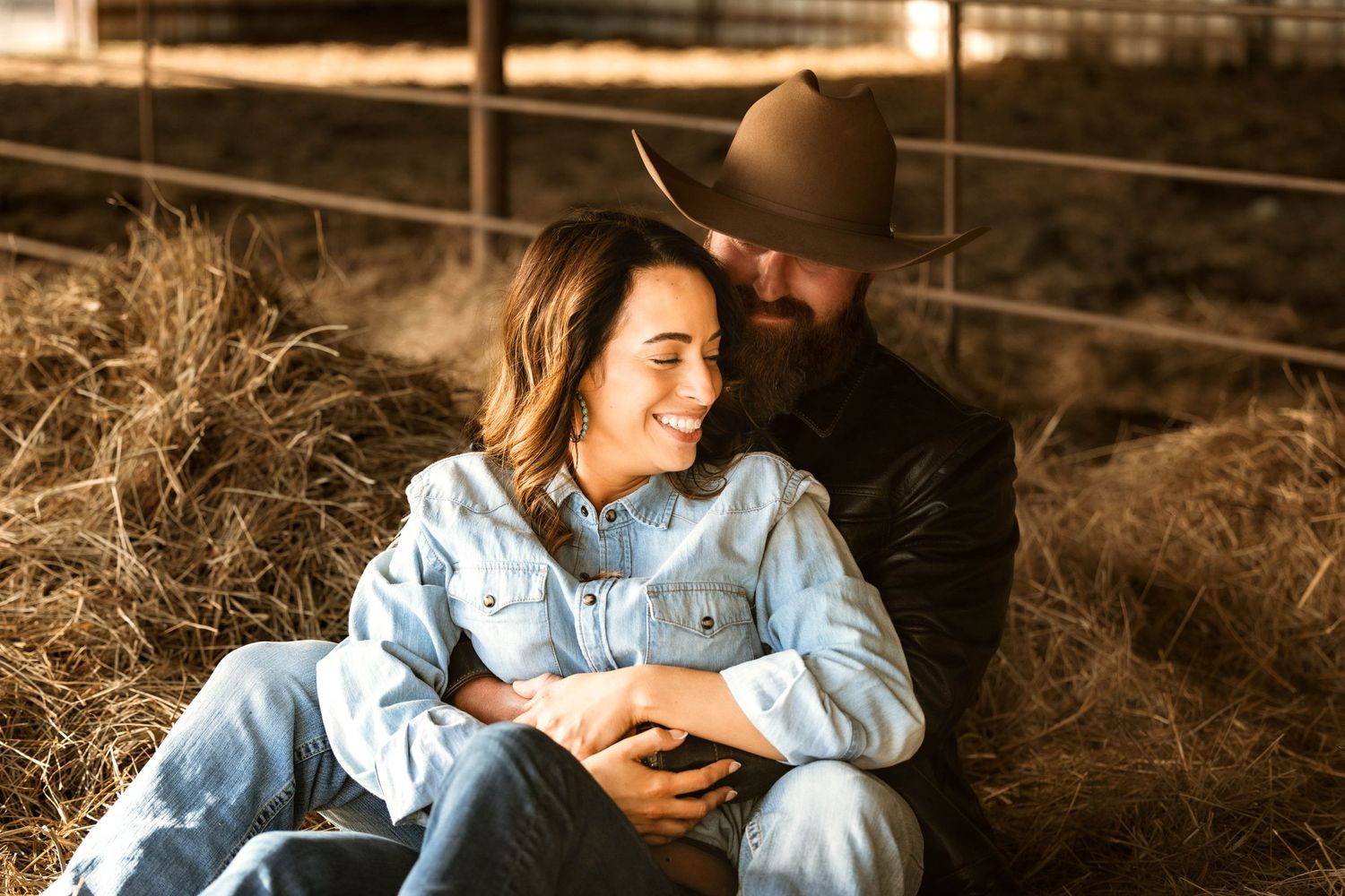 A couple relaxes together on hay bales at golden hour in rustic countryside setting.