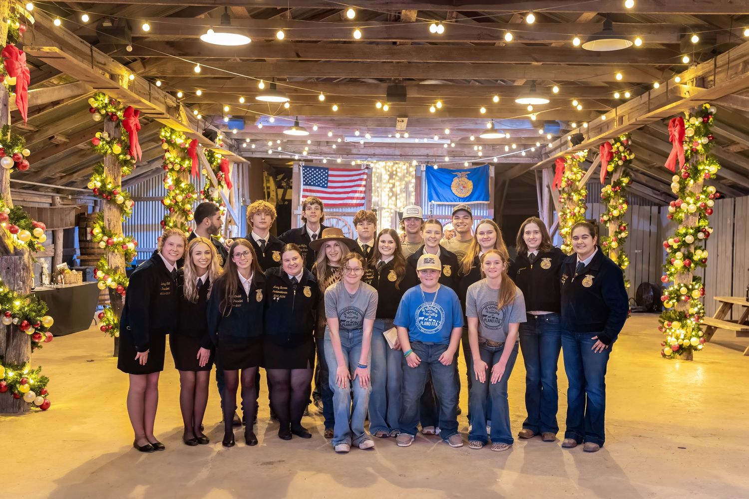 Group photo in decorated barn with string lights and FFA flags.