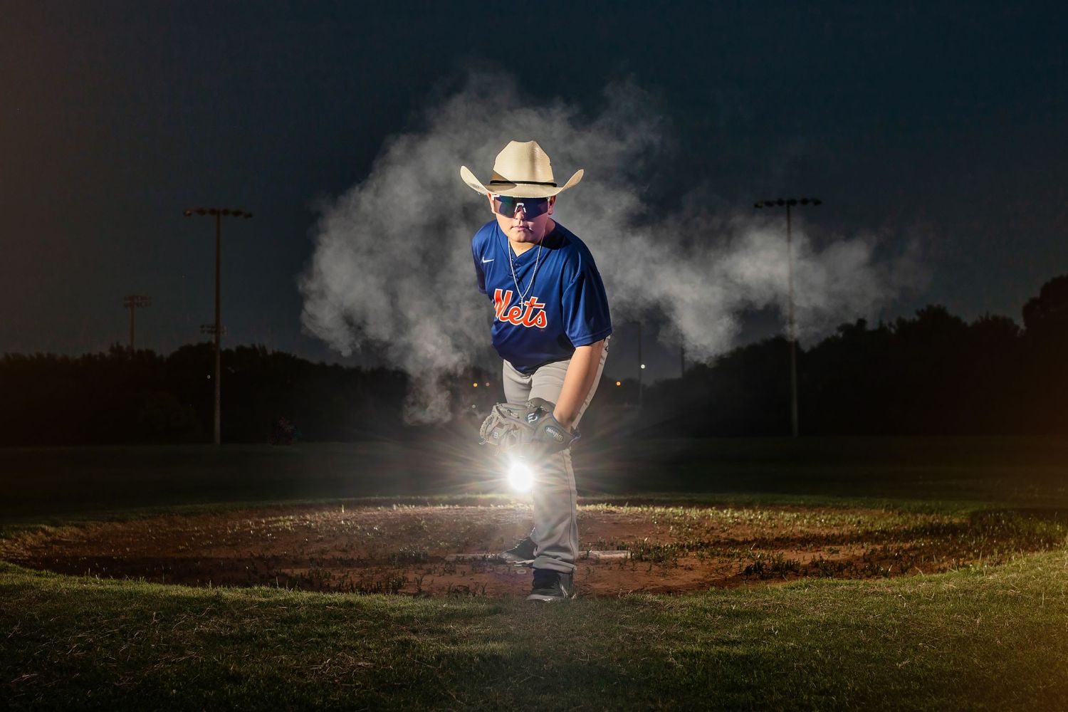 A baseball player in a blue uniform surrounded by dramatic smoke effects on a dark field.