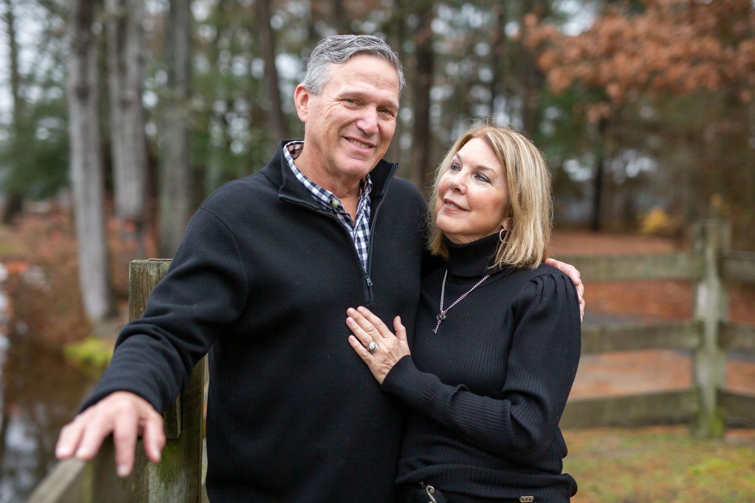 a couple in their 60s at Trap Pond State Park during a family photo session with a fence behind them in fall photography by ashley chance