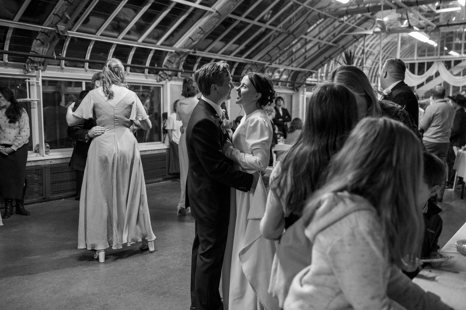 A black and white image of couples dancing at an indoor wedding reception.