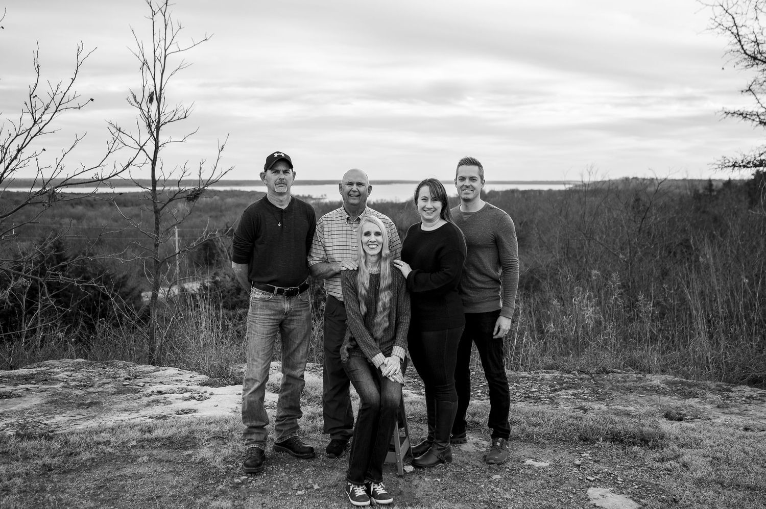 Black and white family portrait of five people posing on rocky overlook with scenic landscape in background.