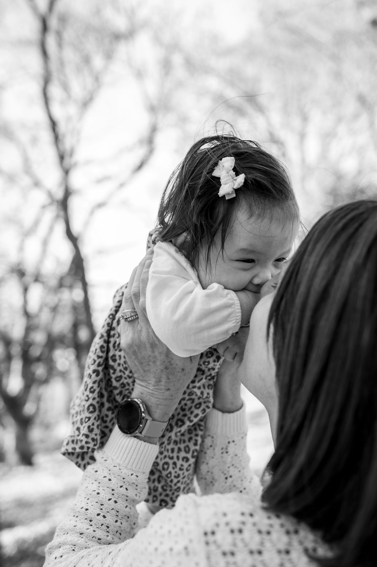 Black and white photo of a mother lifting her smiling baby girl outdoors among bare trees.