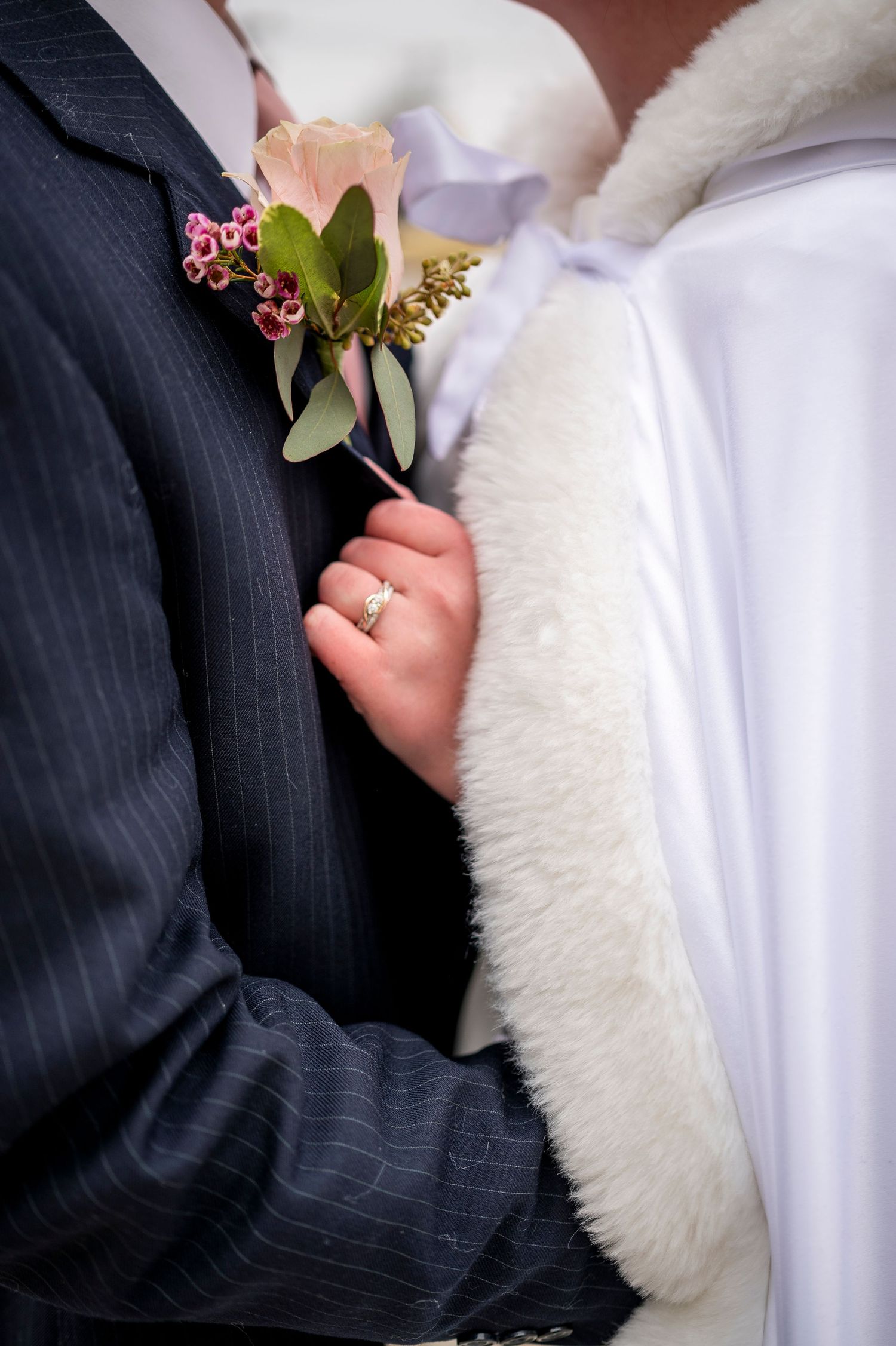 Detailed close-up of a delicate pink and green wedding boutonniere against formal attire.