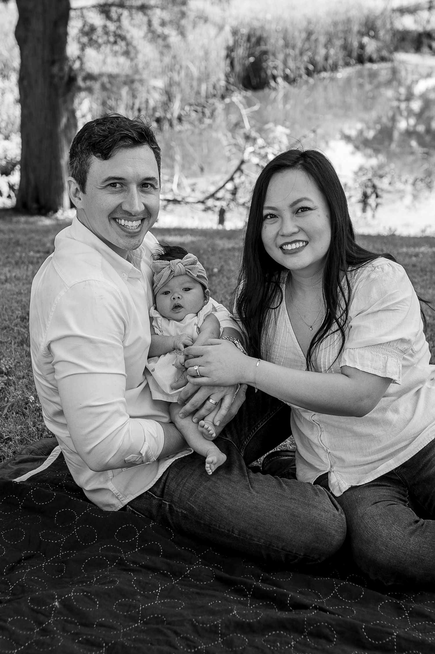 Black and white portrait of a young family sitting together on a blanket outdoors.