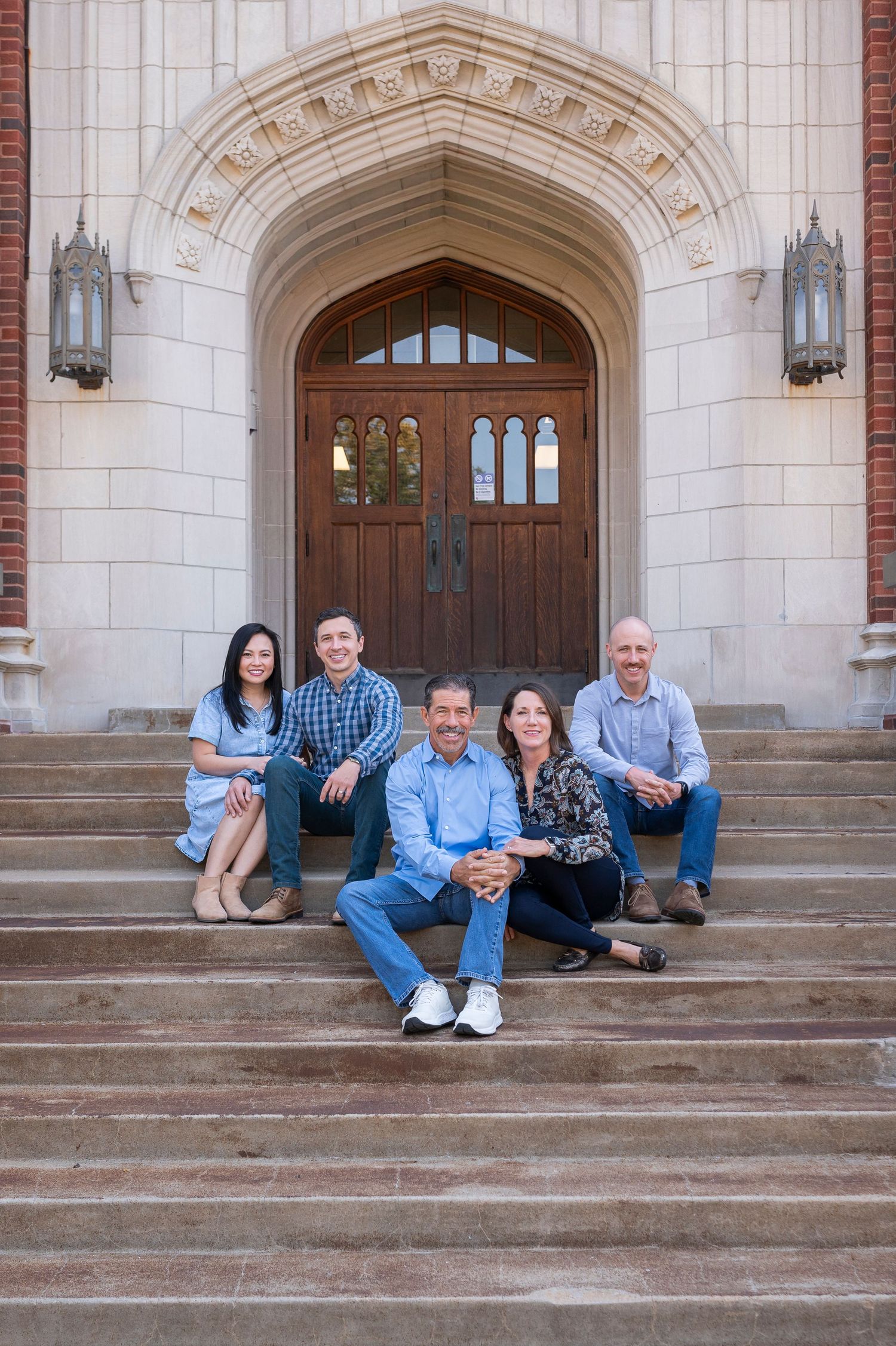 Group sitting on stone steps in front of ornate Gothic archway with lanterns at a university building.