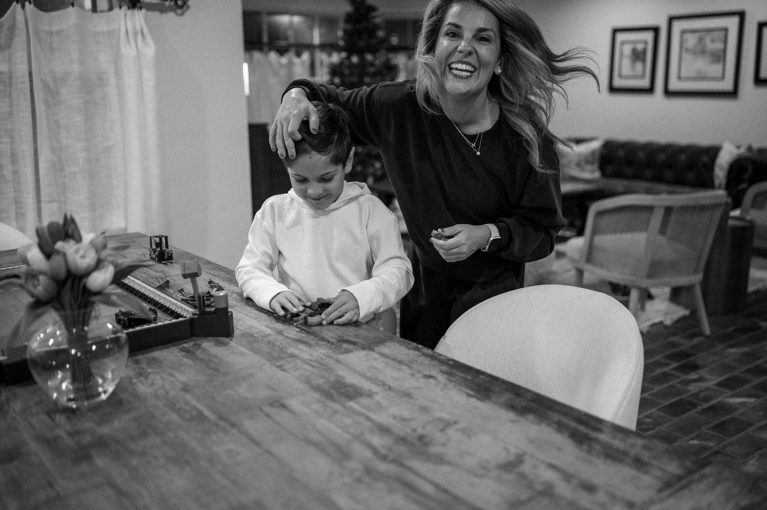A joyful candid moment in the kitchen as two people share laughter at a wooden table.