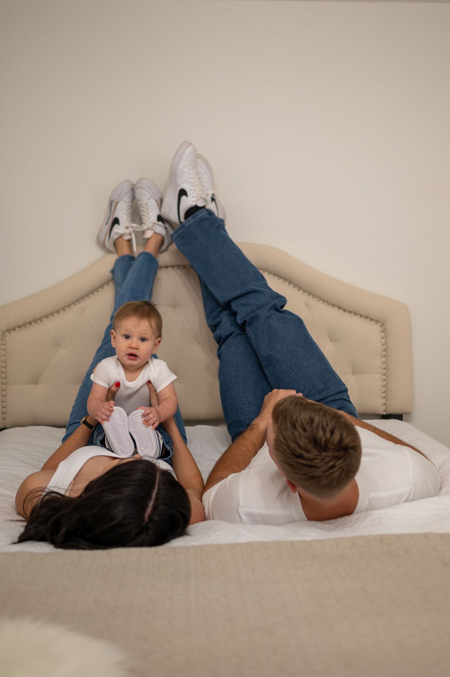 A playful family scene on a beige headboard bed with feet up in casual lifestyle photography.