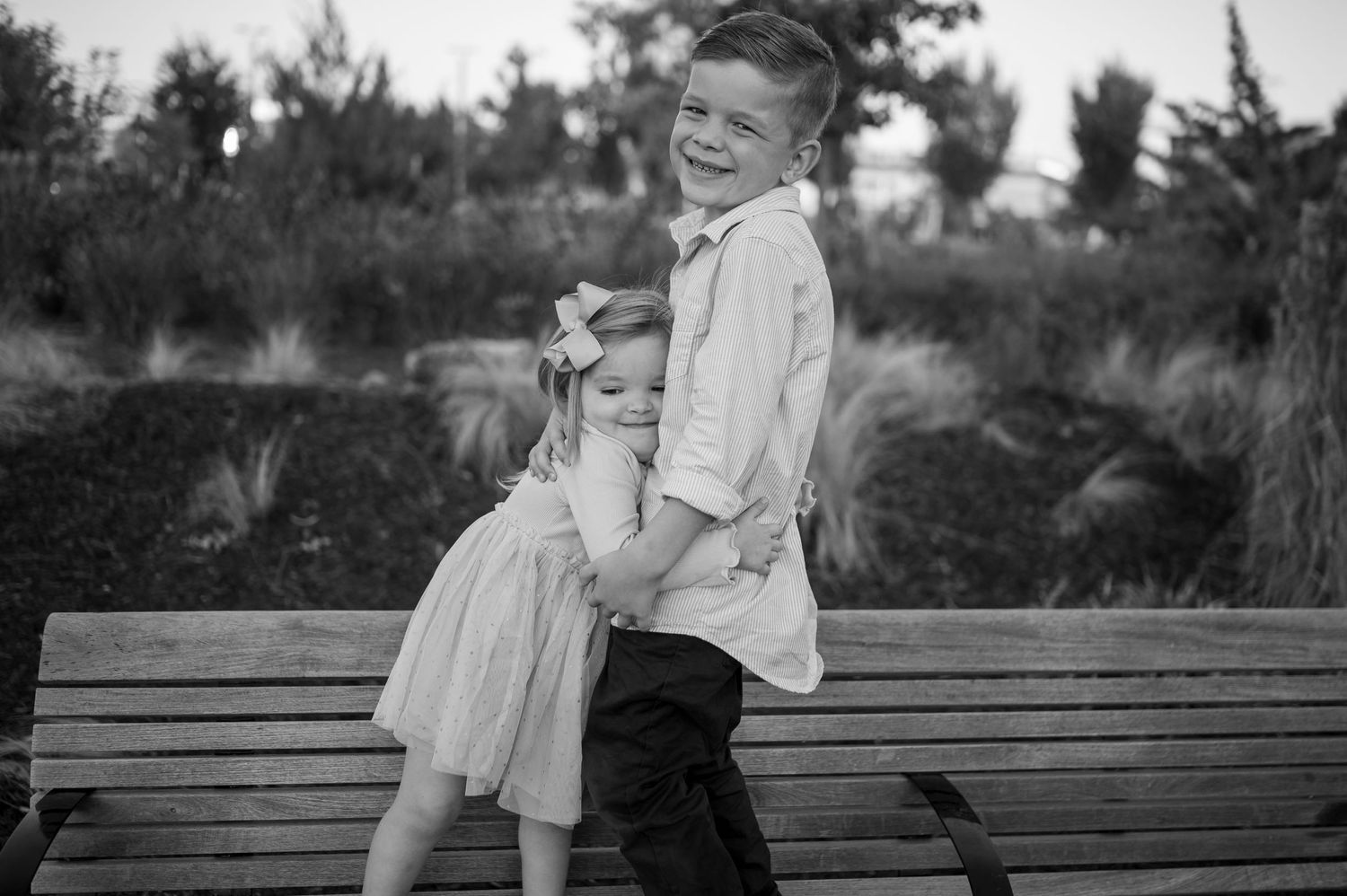 A black and white capture of two children in playful poses on a wooden bench.