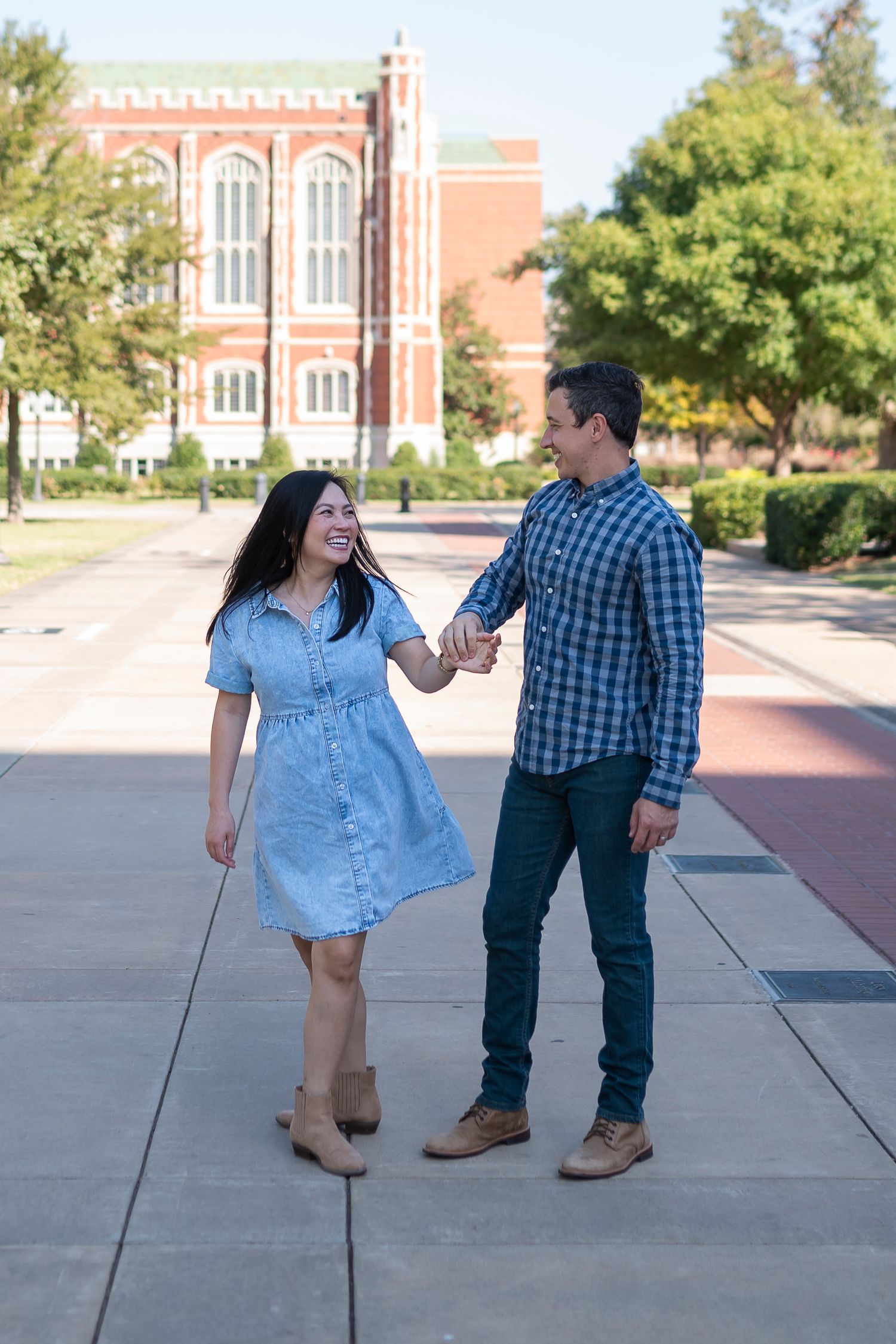 Couple walking and laughing together on campus pathway with collegiate Gothic architecture behind them.