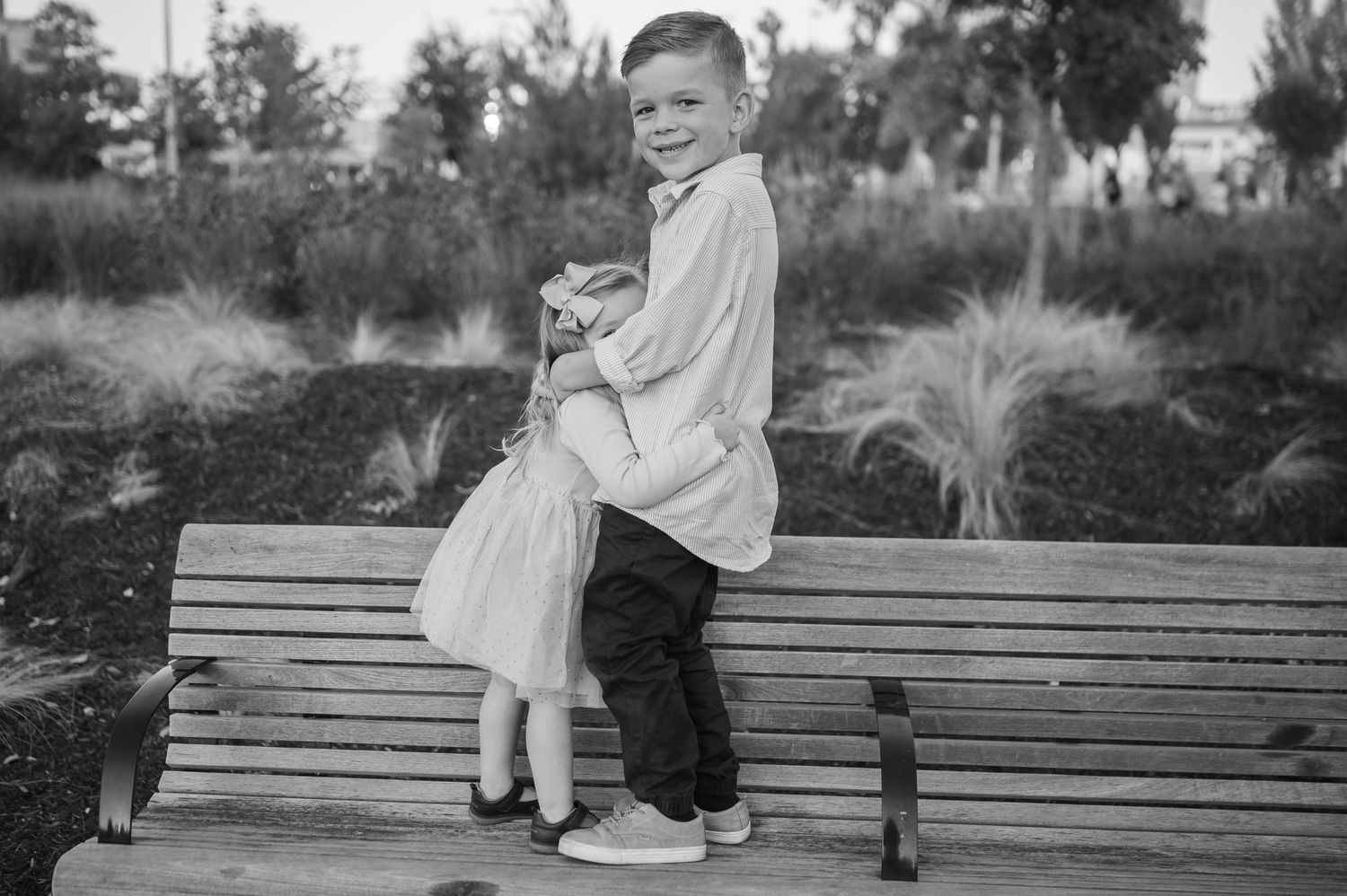 A black and white portrait of two children posing together on a wooden park bench.