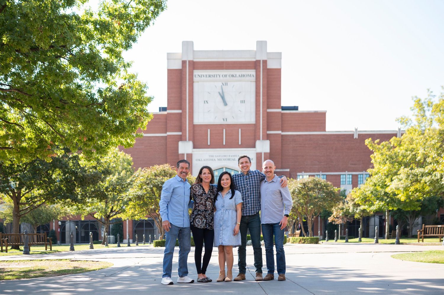 A group poses for a photo in front of a university clock tower on a sunny day.