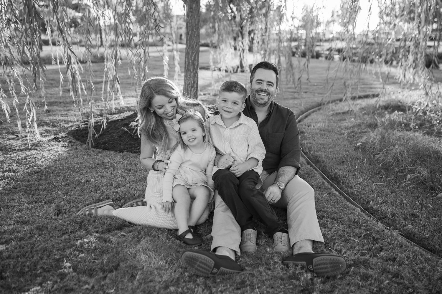 A family sits together on a fallen tree trunk in a wooded setting.