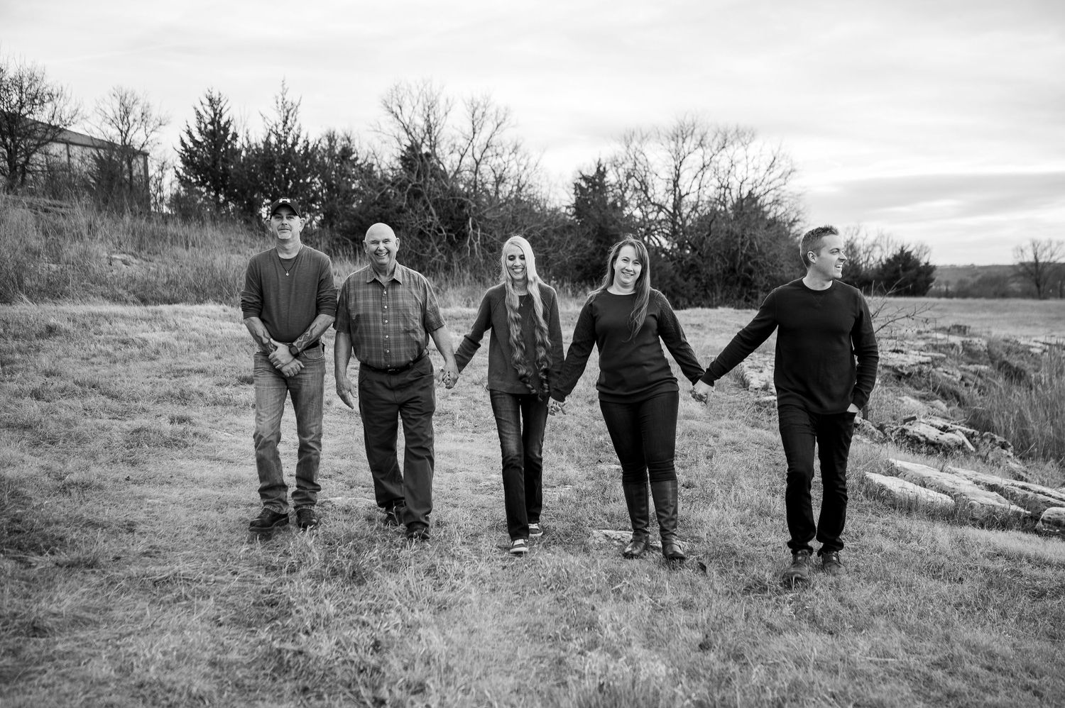 Black and white photo of five people holding hands in a field, posing for a family portrait outdoors.