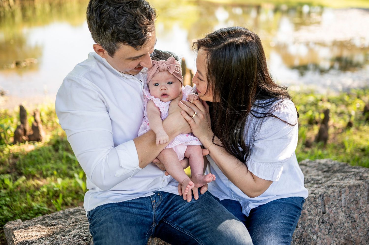 Family enjoys quality time together on stone ledge by pond in park setting.
