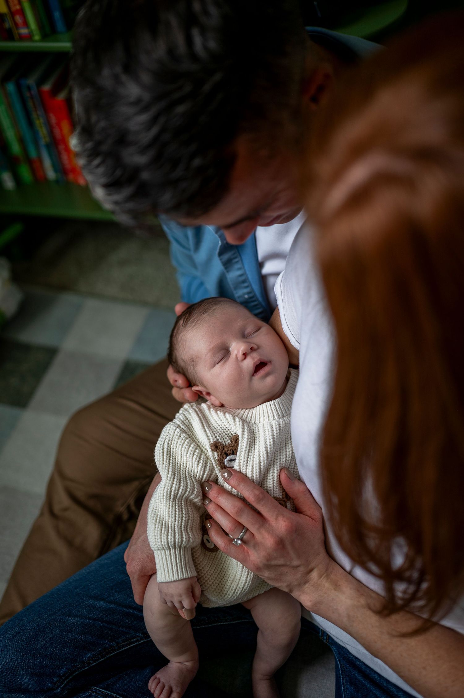 A newborn baby sleeps peacefully while parents lovingly cradle it in their arms.