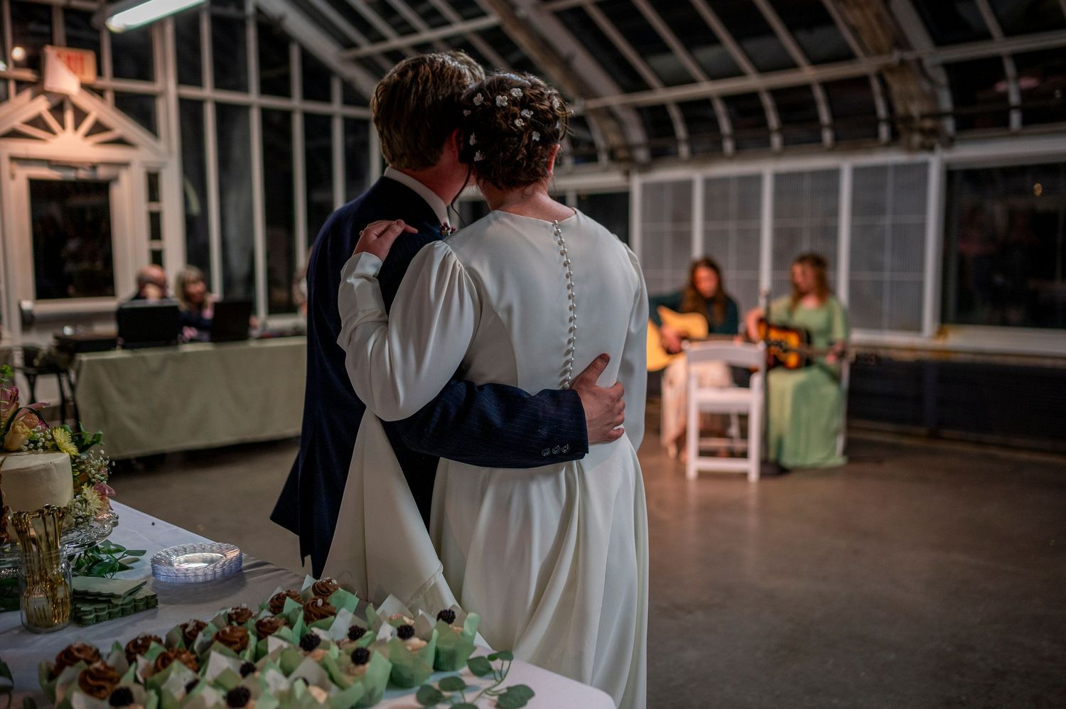 A couple embraces during their wedding reception in a beautifully lit greenhouse venue.