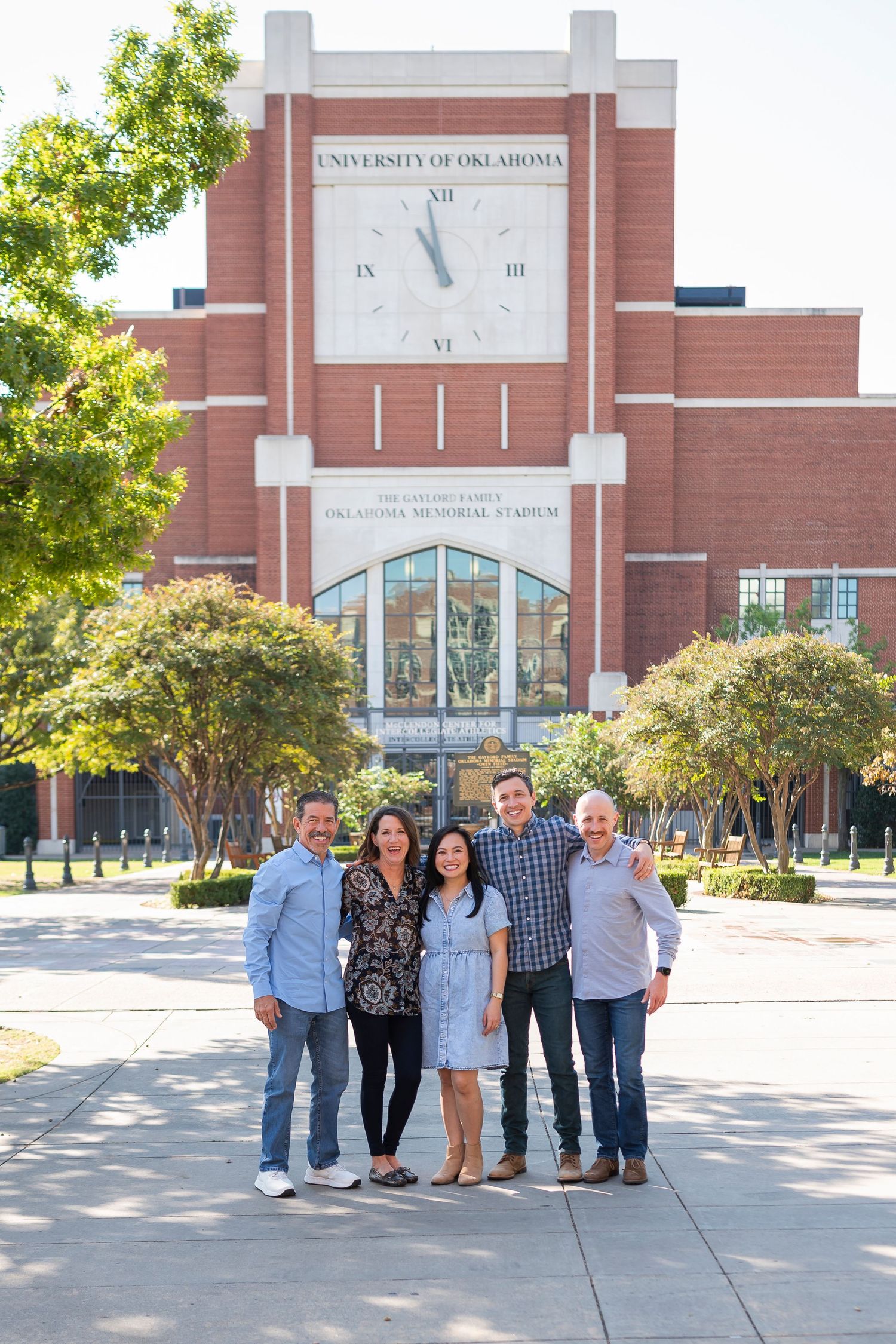 A group poses together in front of a university building with a clock tower and brick facade.