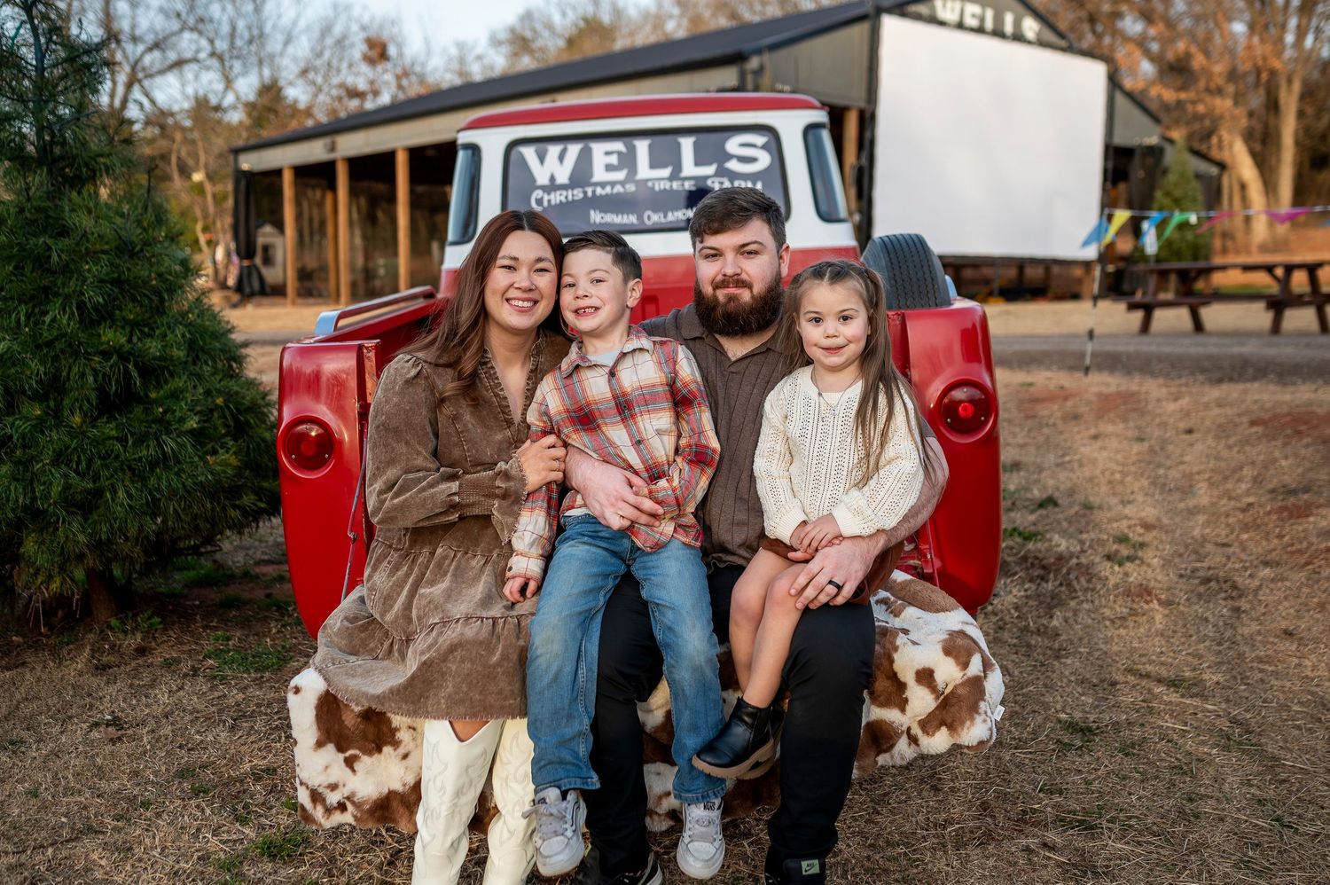 Family of four smiling together in the bed of a vintage red Wells truck outdoors.