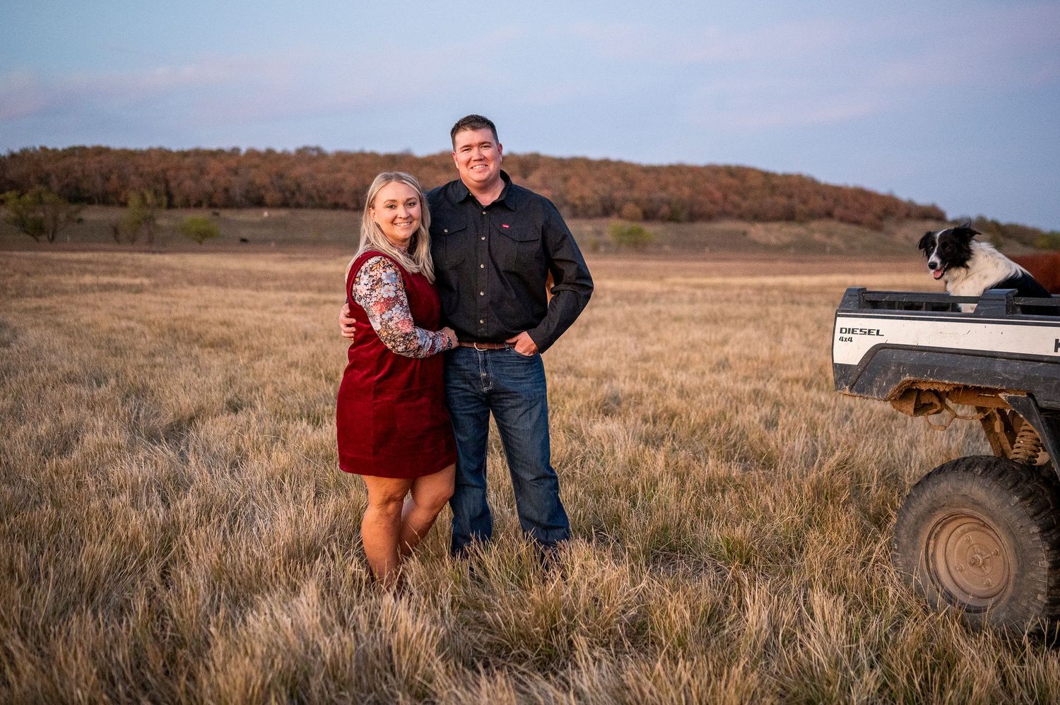 Couple posing together in a golden field beside an ATV with colorful autumn hills in the background.