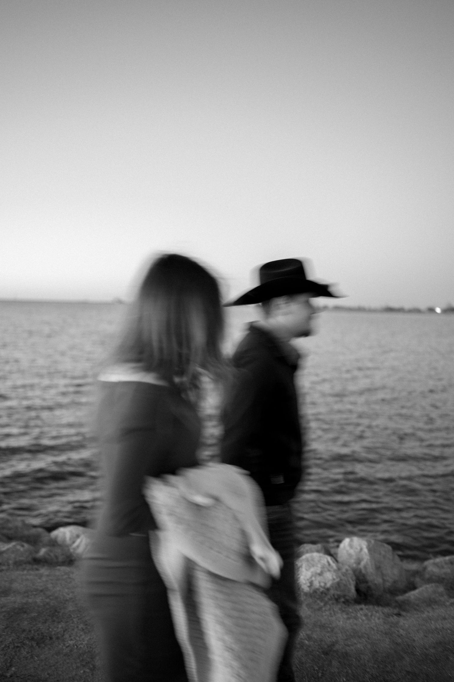 An artistic black and white blurred photo of figures by the water at sunset.