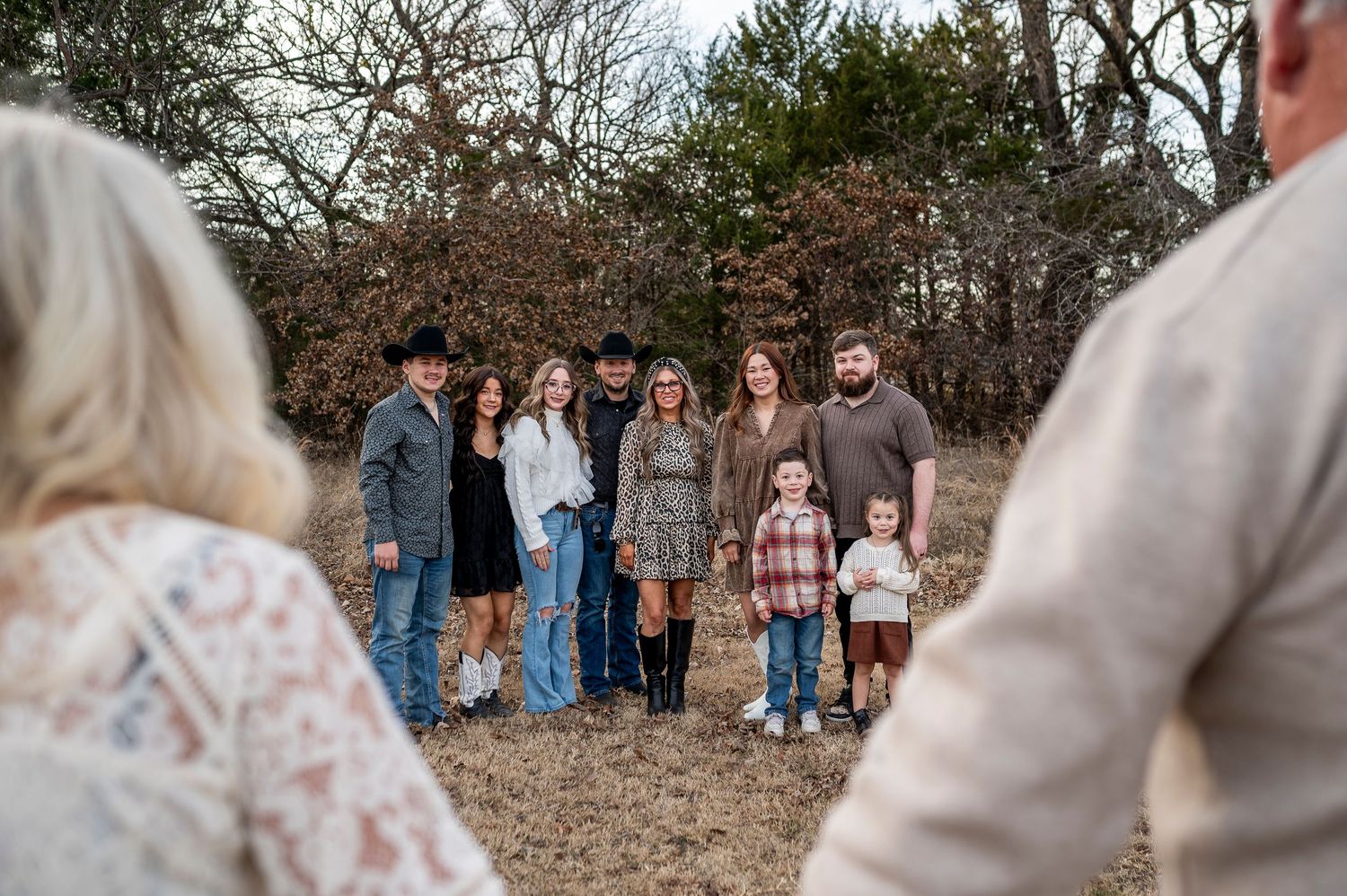 Family group portrait outdoors in winter, posing together in a field with bare trees in the background.