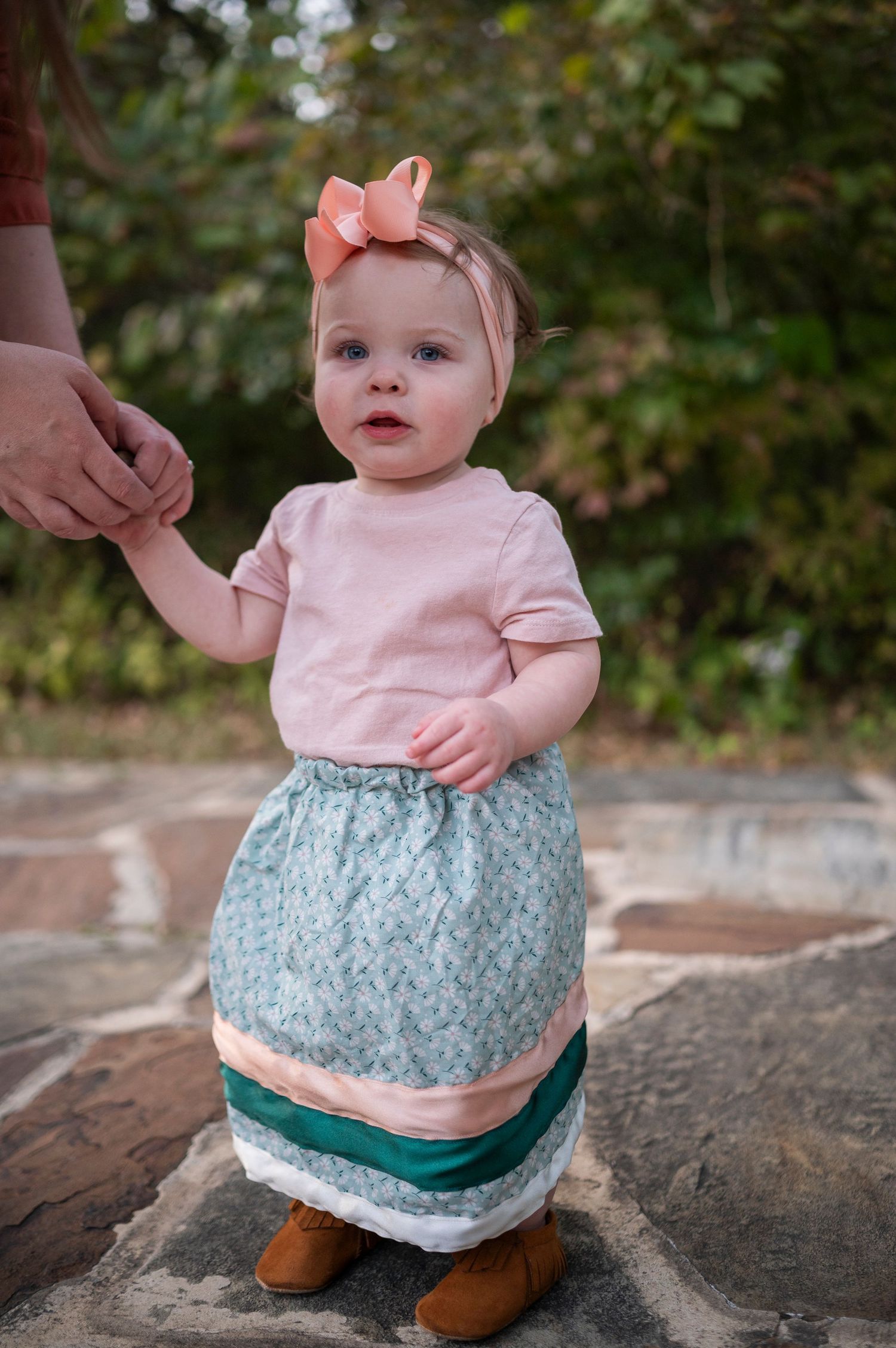 Small child in pink top and patterned skirt standing on stone surface outdoors.