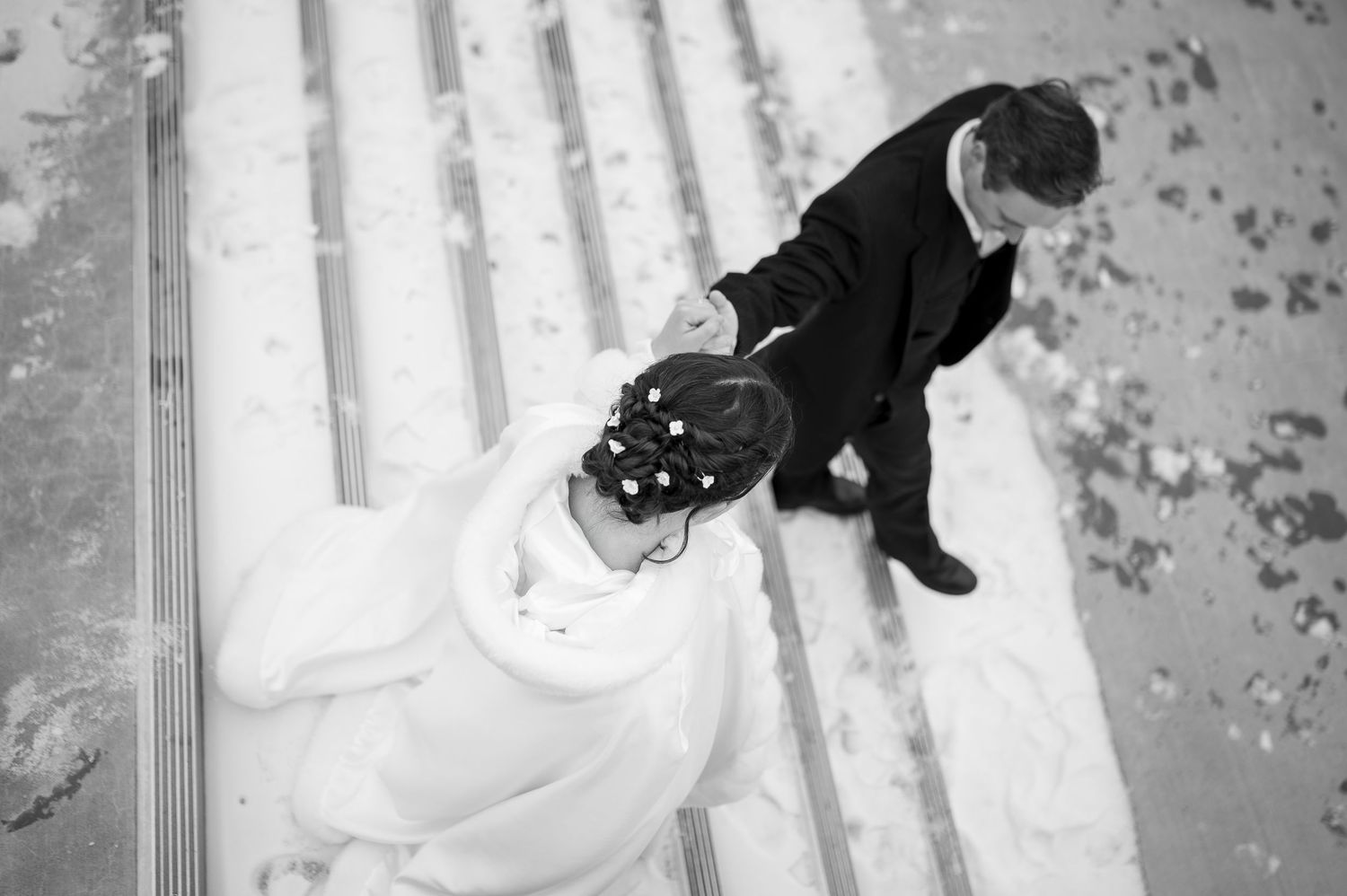 An artistic black and white overhead shot of a couple in wedding attire on stone steps.