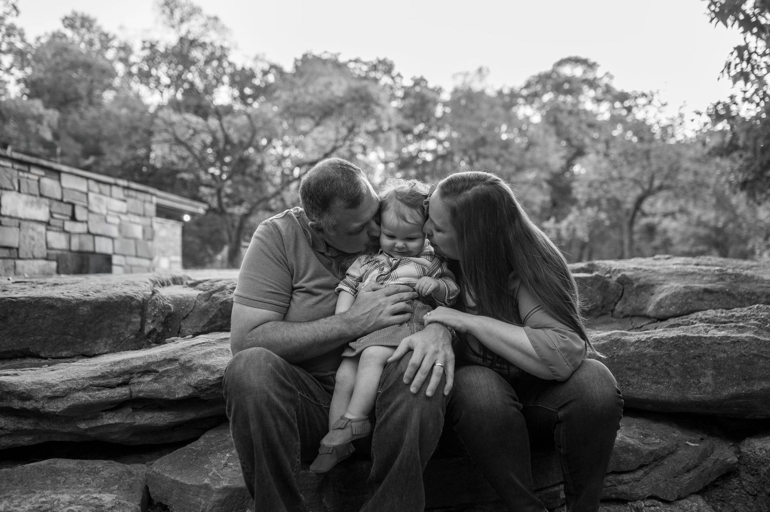 Intimate black and white family moment captured on stone wall outdoors.