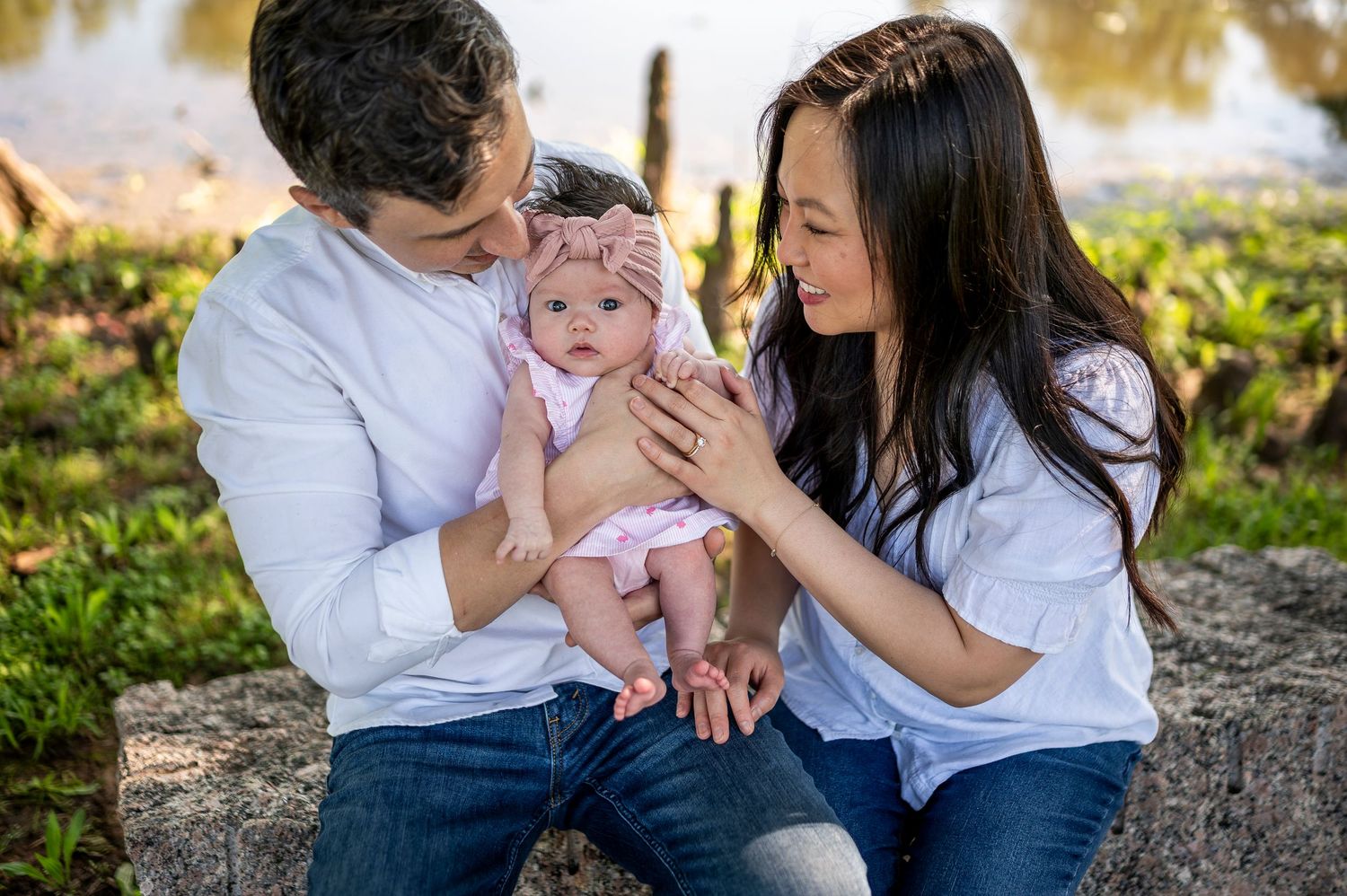 Family shares intimate moment with baby in pink outfit at sunset in park setting.
