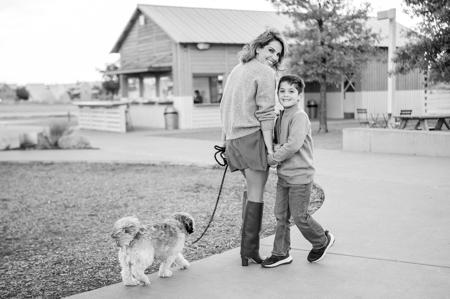 Black and white photo of a woman and boy walking a fluffy dog on a leash in a park setting.