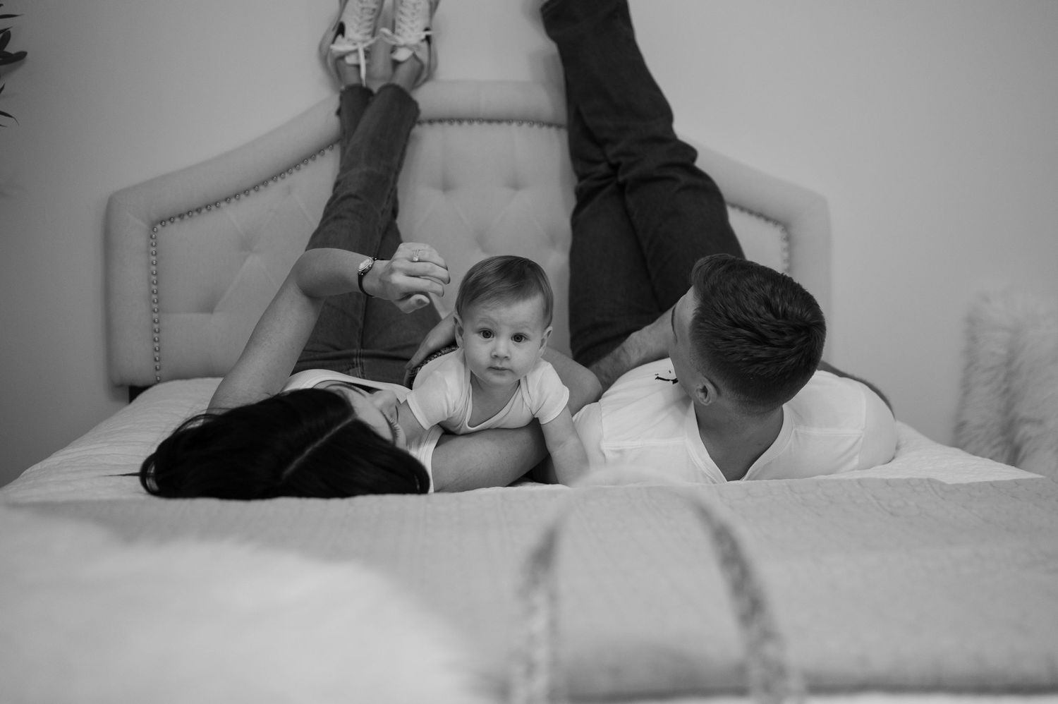 A playful family moment on a beige upholstered bed in black and white photography.
