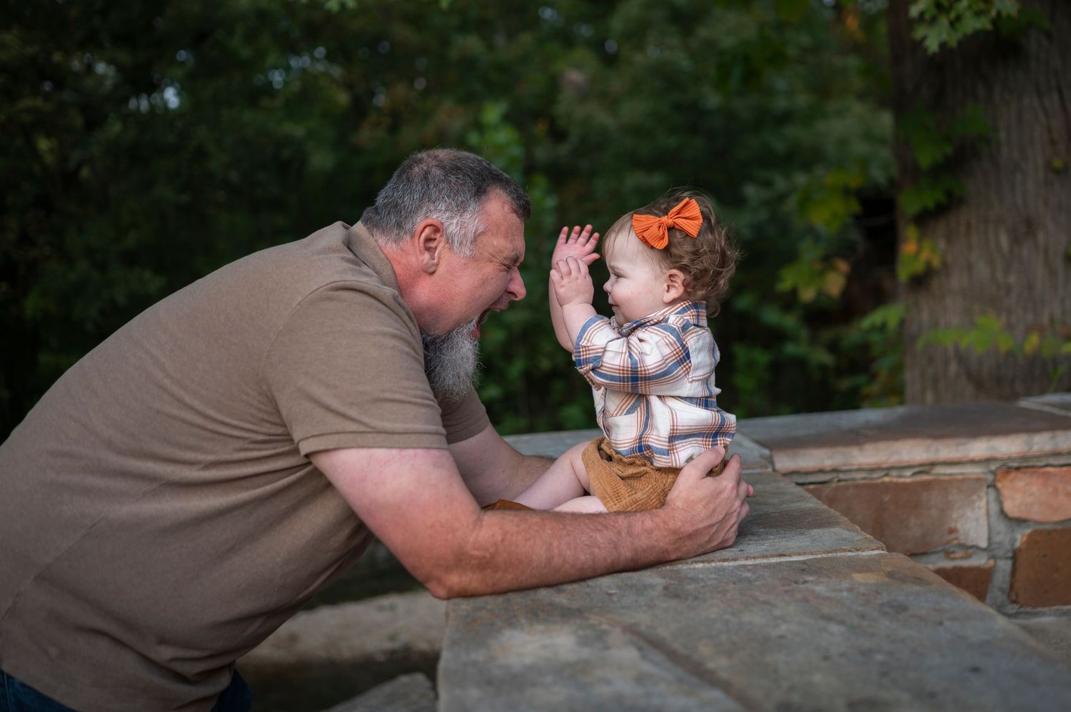 Playful outdoor moment between adult and small child at rustic wooden table.