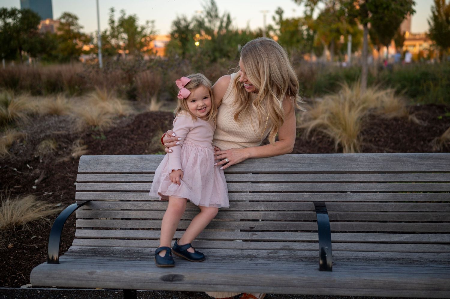 A tender moment shared between two people on a wooden bench at sunset with city buildings in background.