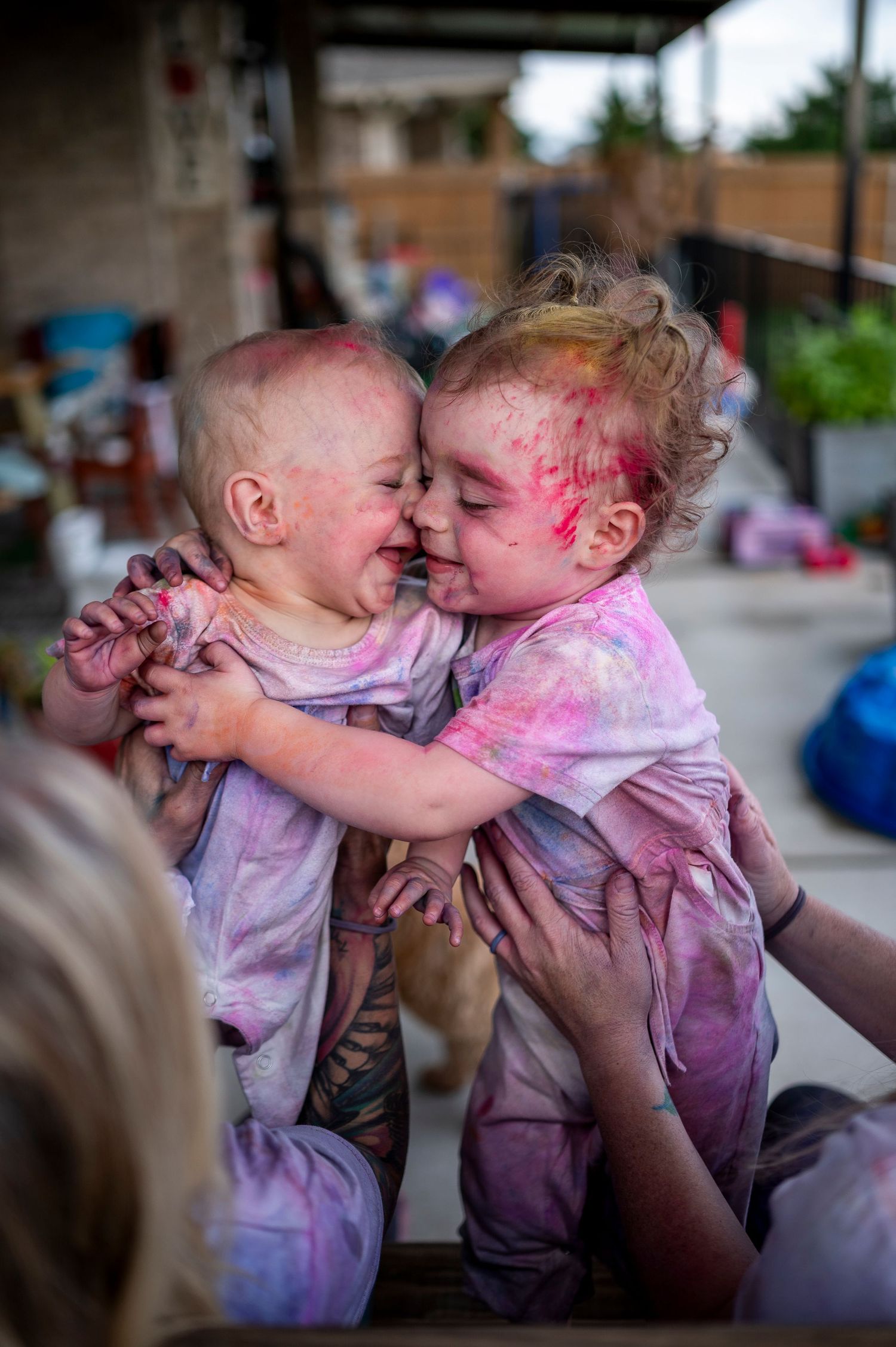 Two young children covered in pink powder embrace during a colorful Holi festival celebration.