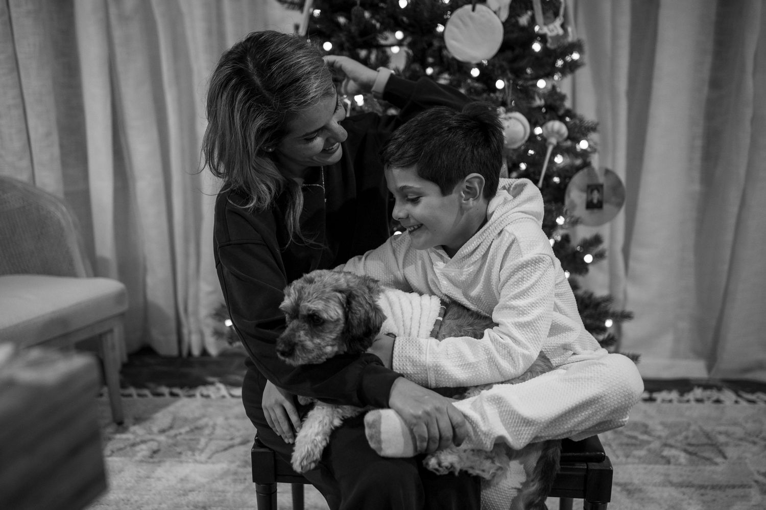 Black and white portrait of a family with their small dog by a Christmas tree.