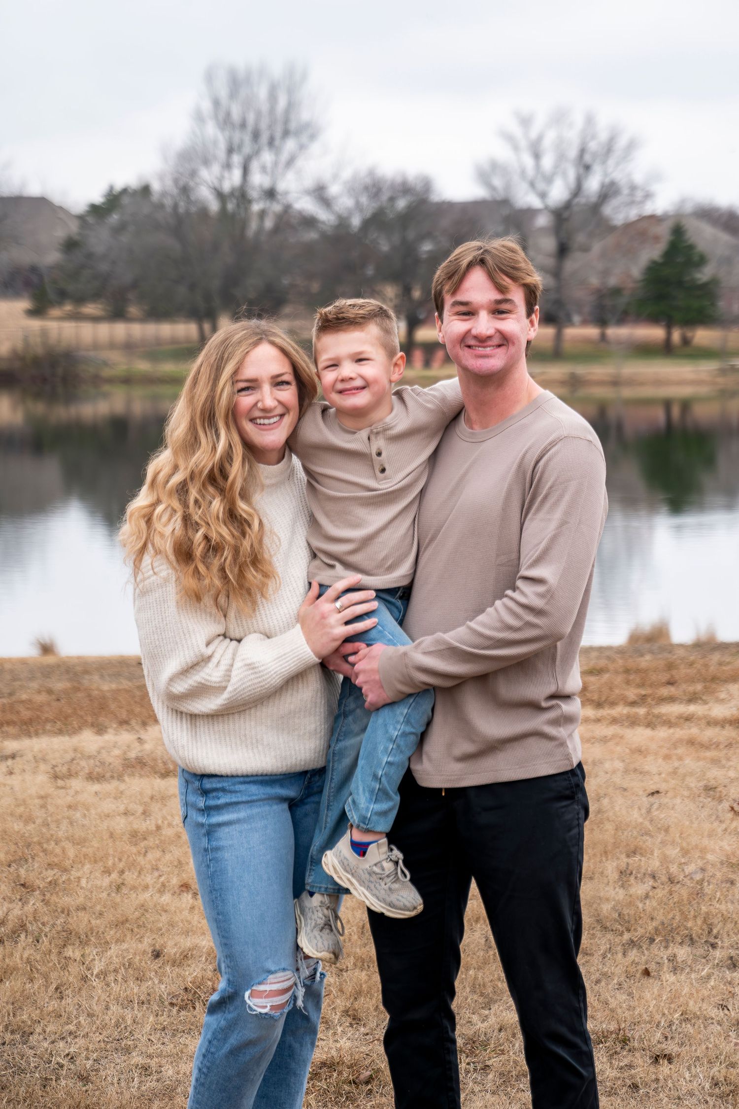 A happy family portrait taken near a lake on a cloudy day.