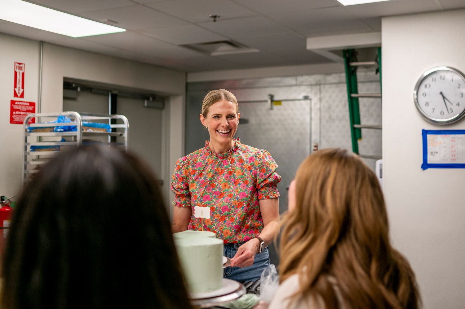A teacher in a colorful patterned shirt stands at the front of a classroom speaking to students.