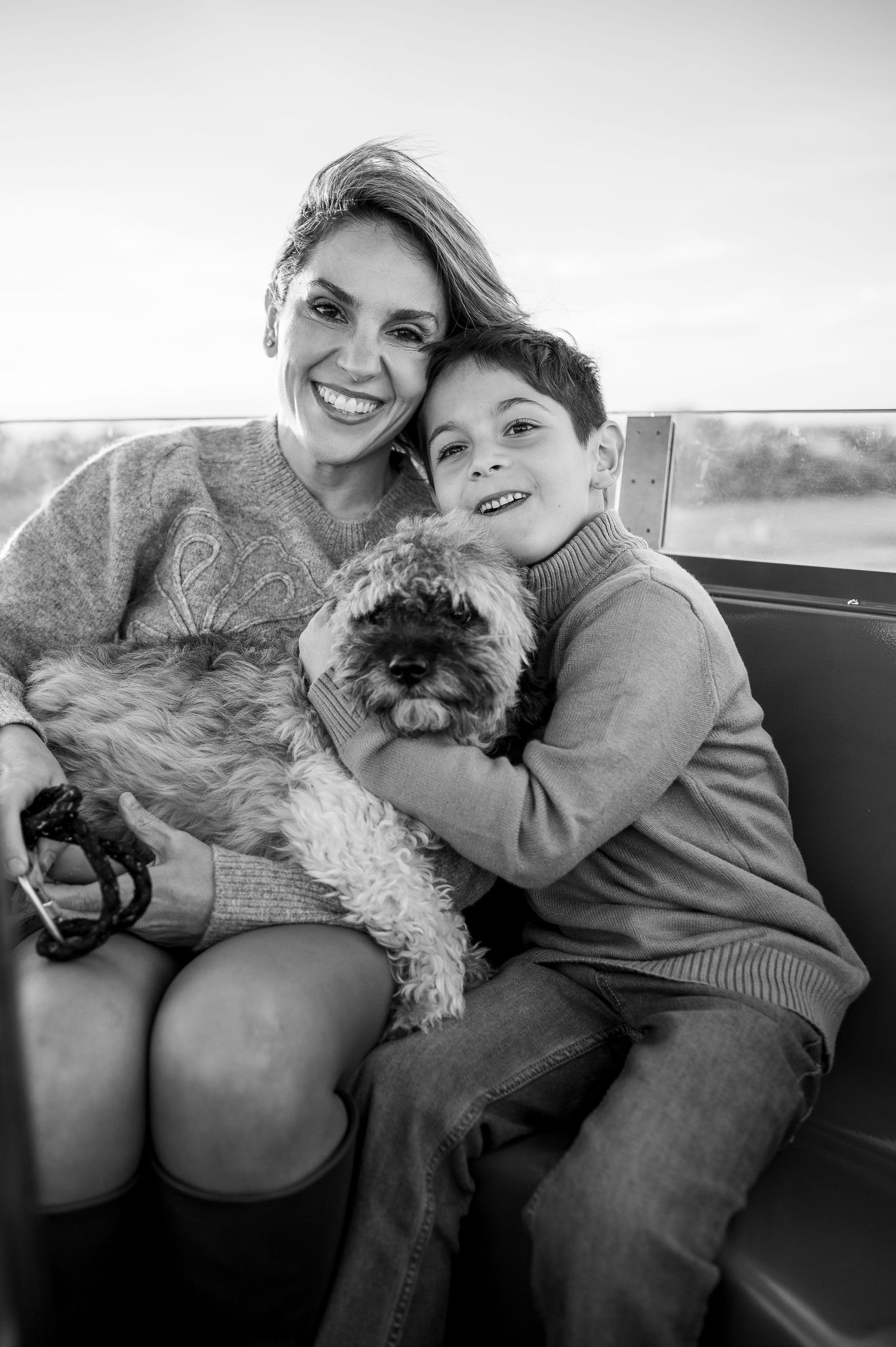 Black and white portrait of smiling woman and boy holding fluffy dog while sitting together outdoors.