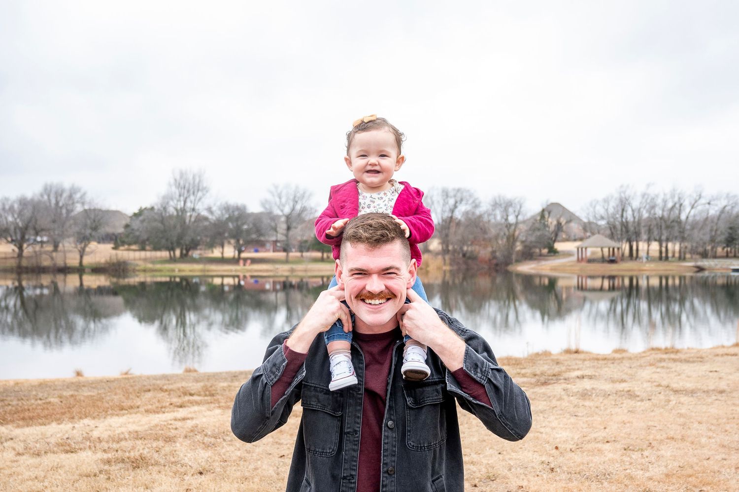 Parent and child having fun together by a serene lake on a cloudy winter day.