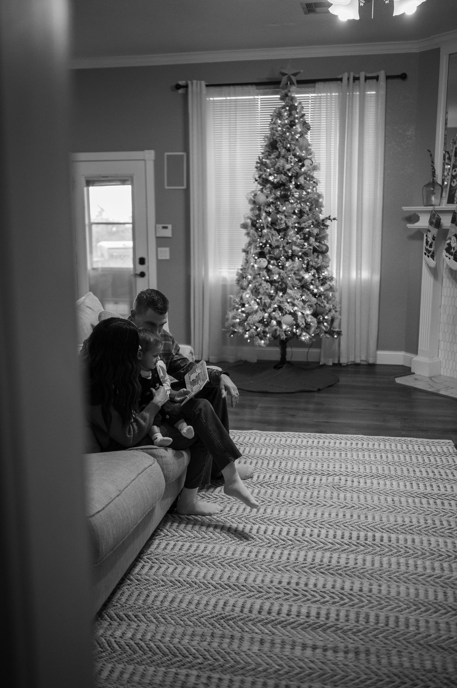 A cozy living room scene with illuminated Christmas tree and people relaxing on sofa.
