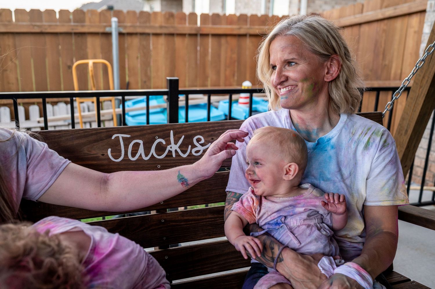 A relaxing moment on a wooden porch swing by a pool with a baby in pink clothing.